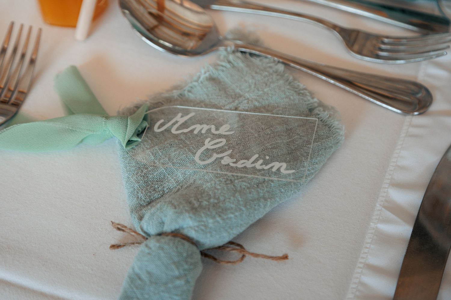Elegant wedding place setting with sage green linen napkin and handwritten calligraphy name card.