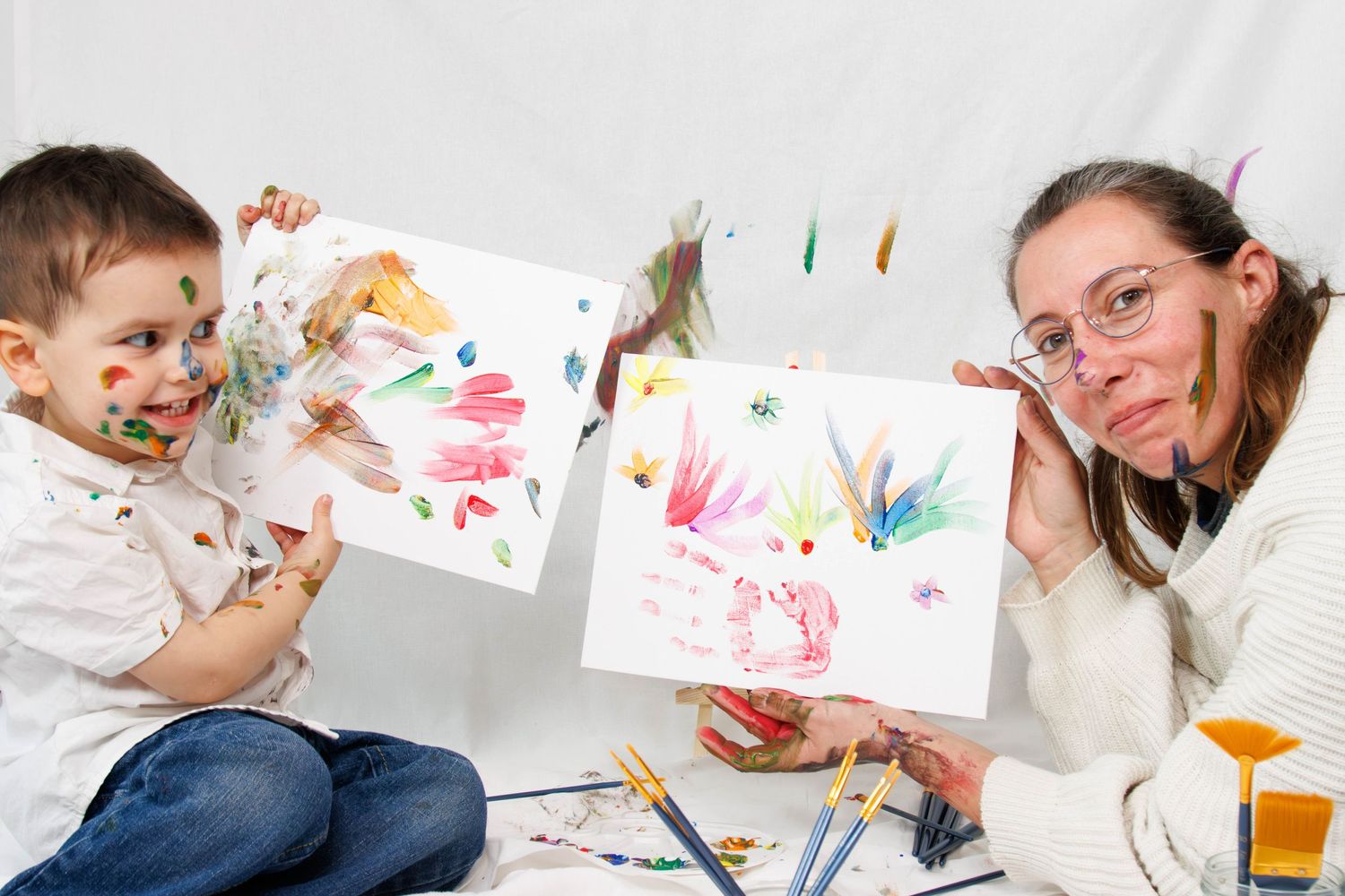 Paint-covered hands displaying colorful artwork during creative painting session.