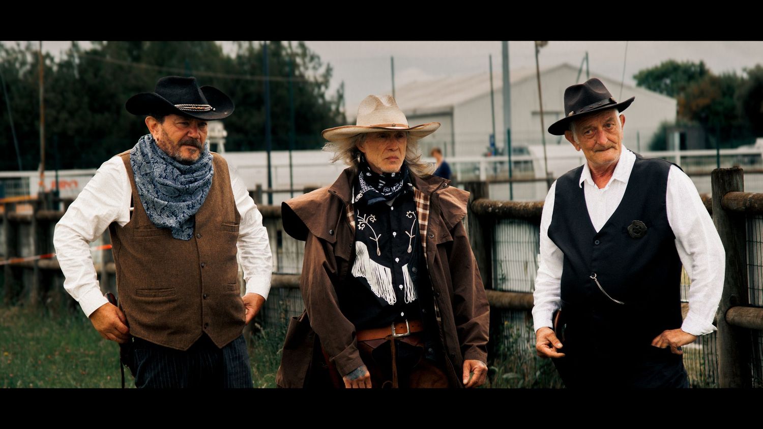 Three cowboys in period dress stand together in western outfits with bandanas.