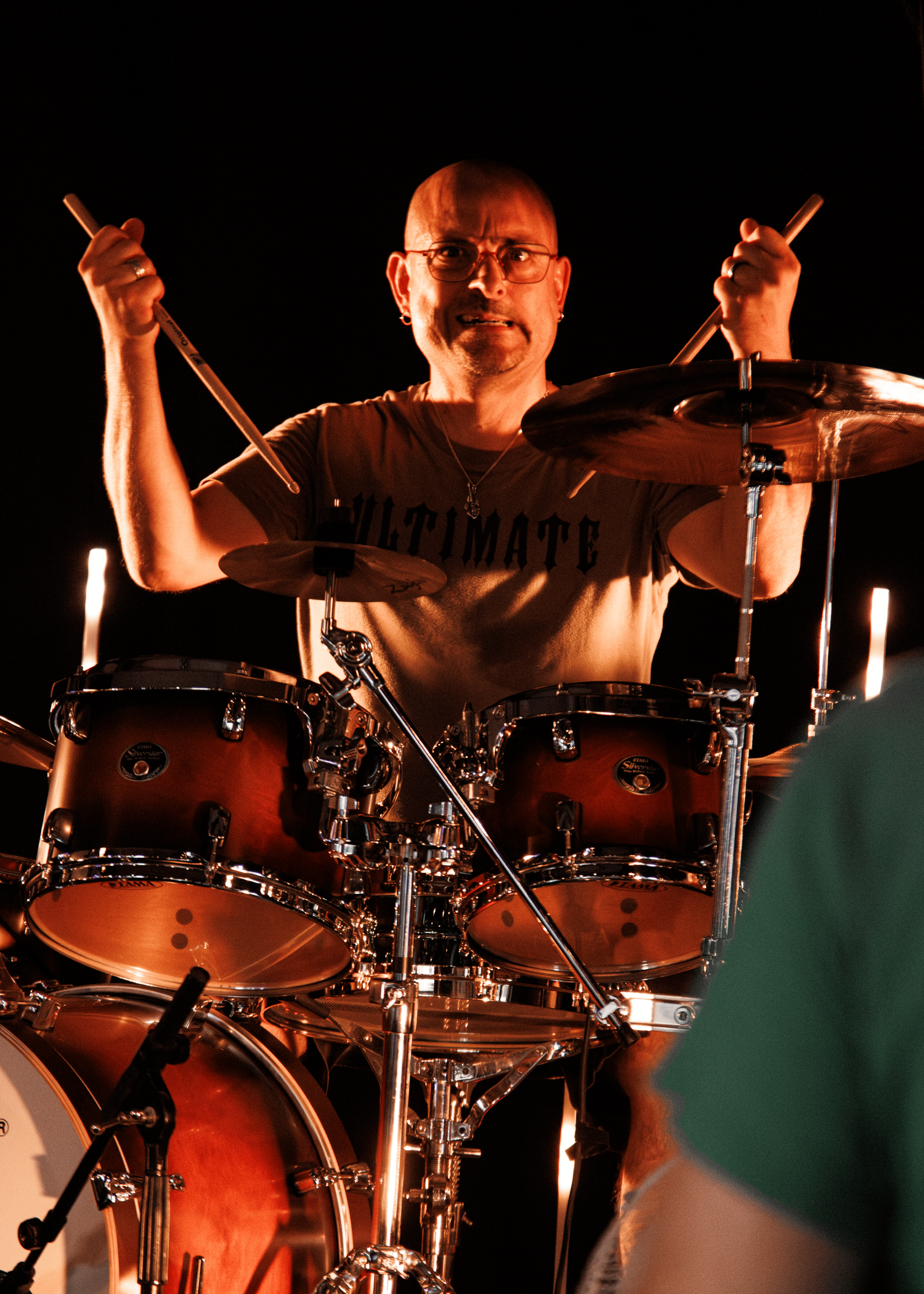 Drummer performing on stage with dramatic lighting and multiple cymbals visible.