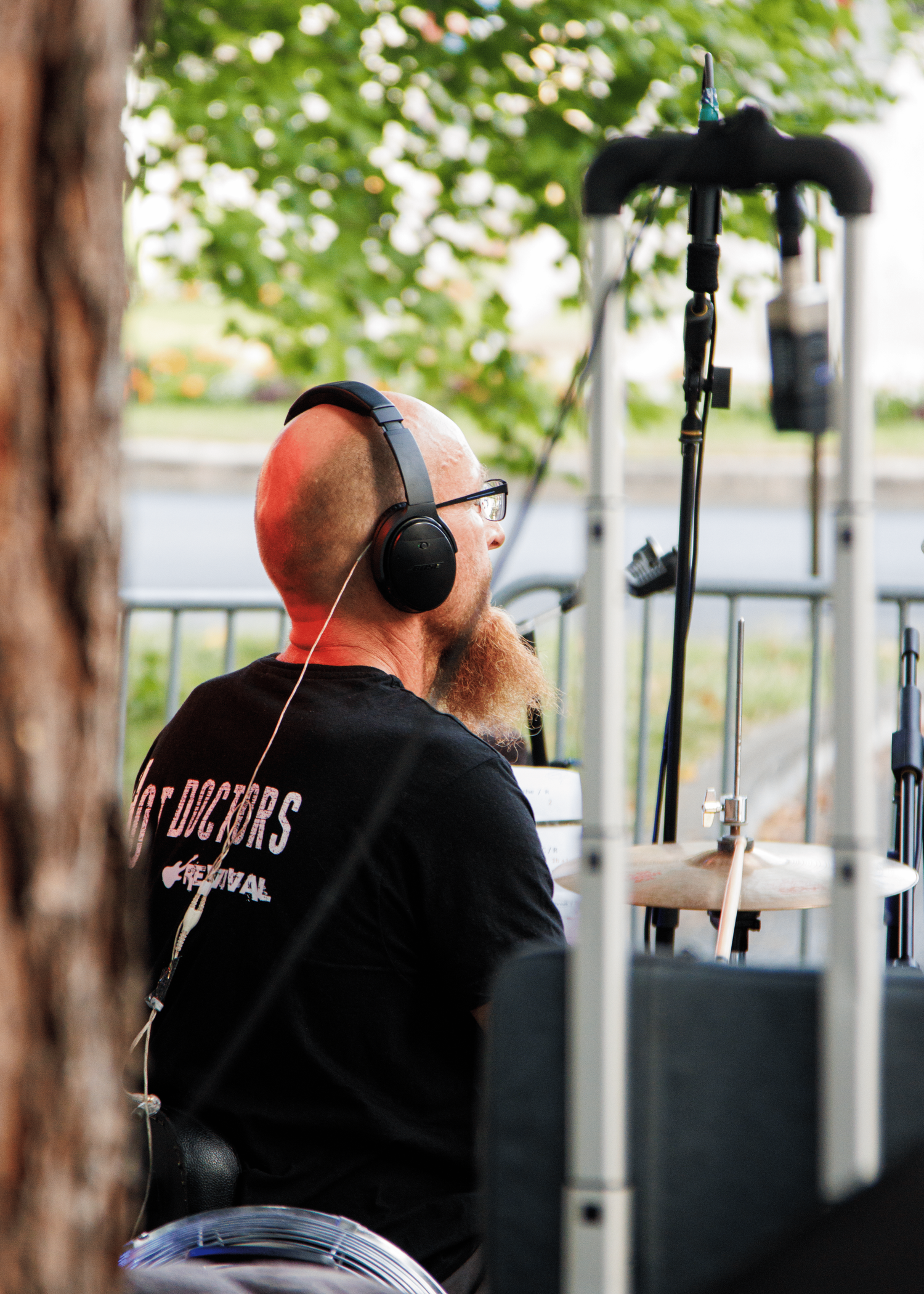 Band member wearing headphones and black t-shirt performing at outdoor concert.