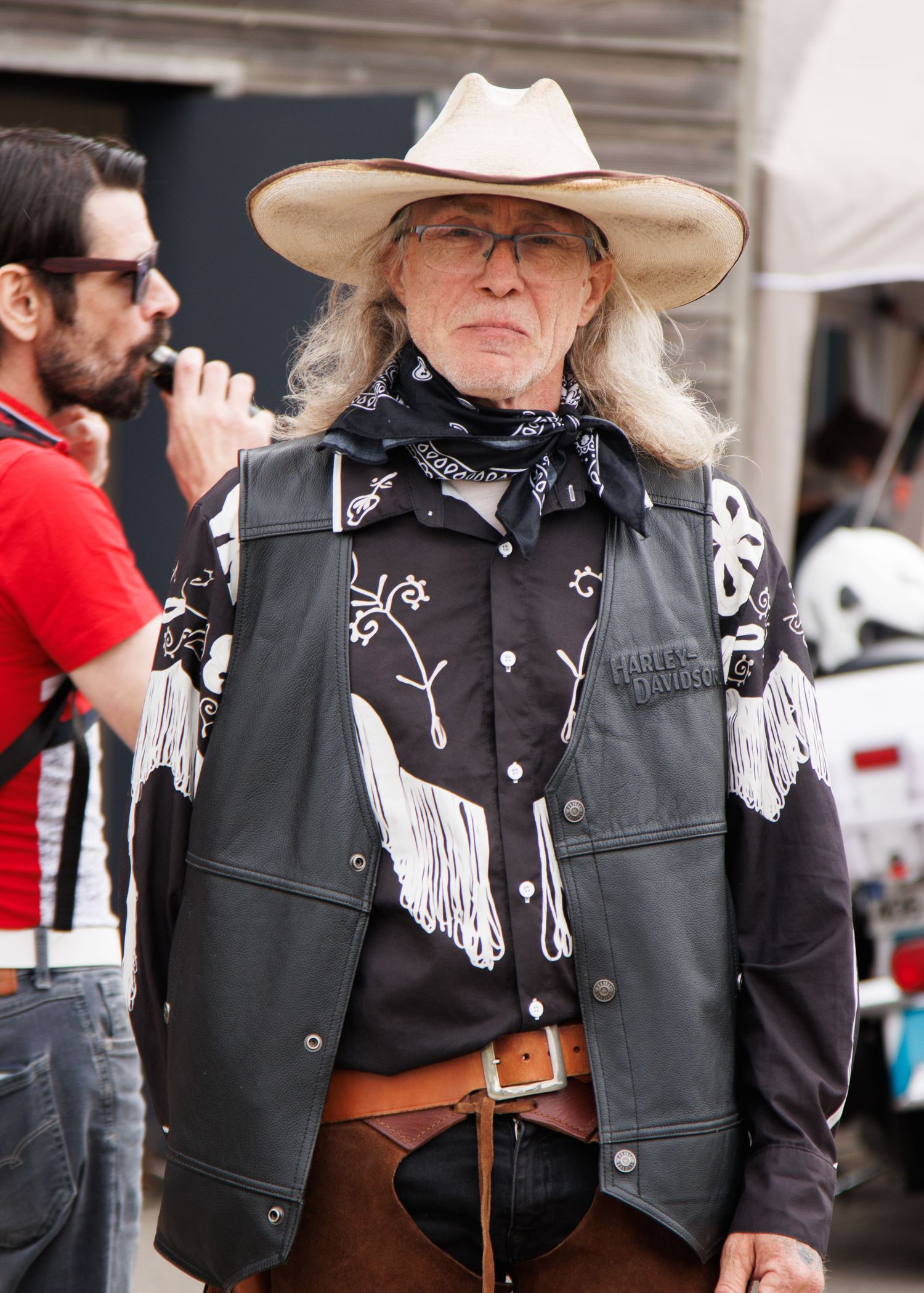 Person in western attire with leather vest and cowboy hat at outdoor event.