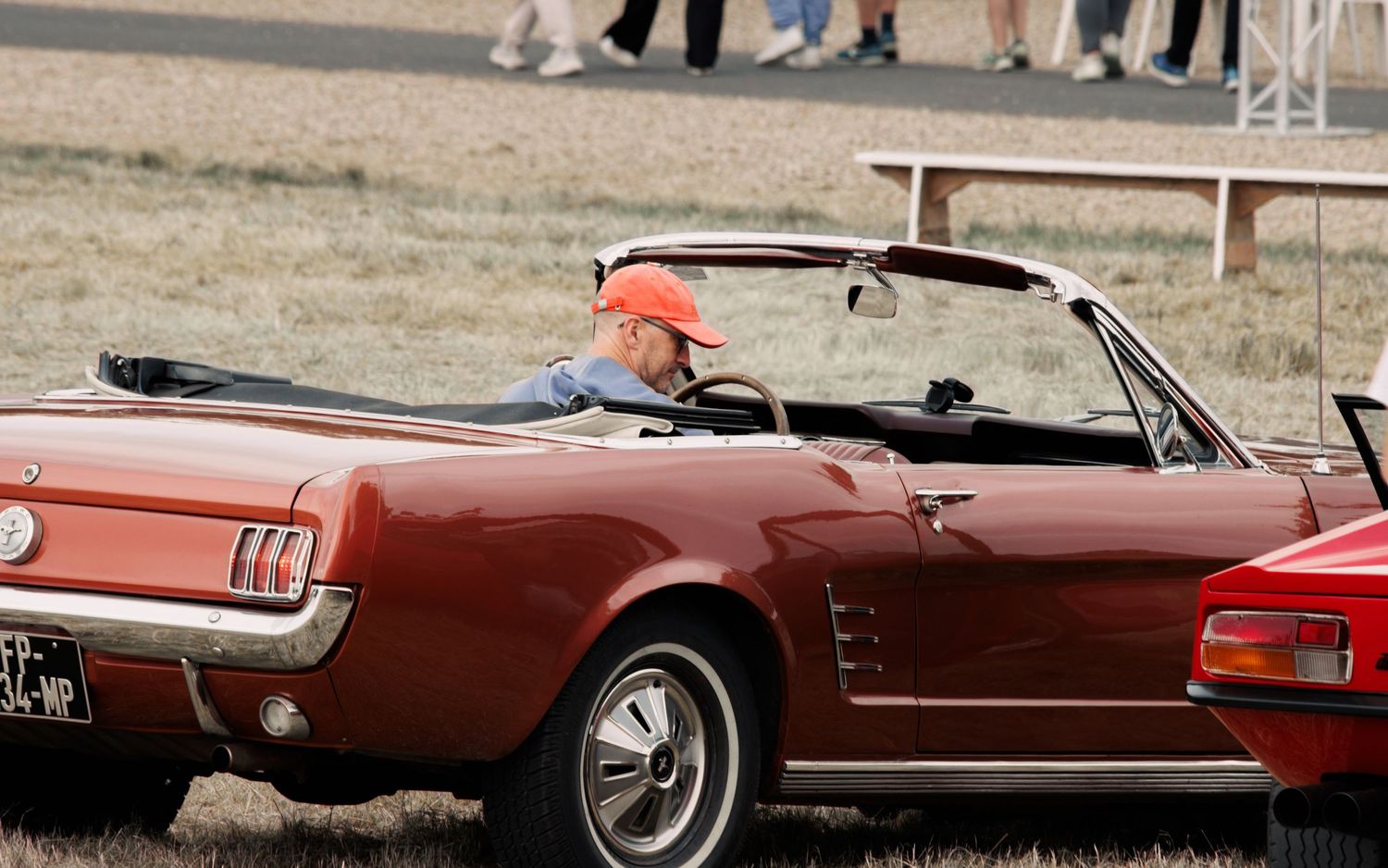 Classic burgundy Ford Mustang convertible parked at outdoor event.
