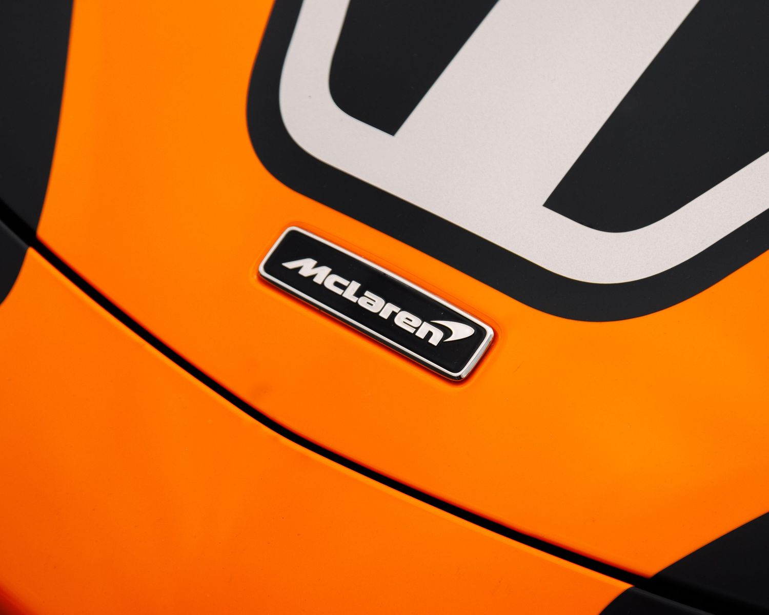 Close-up detail shot of an orange McLaren sports car exterior panel with bold black lettering.