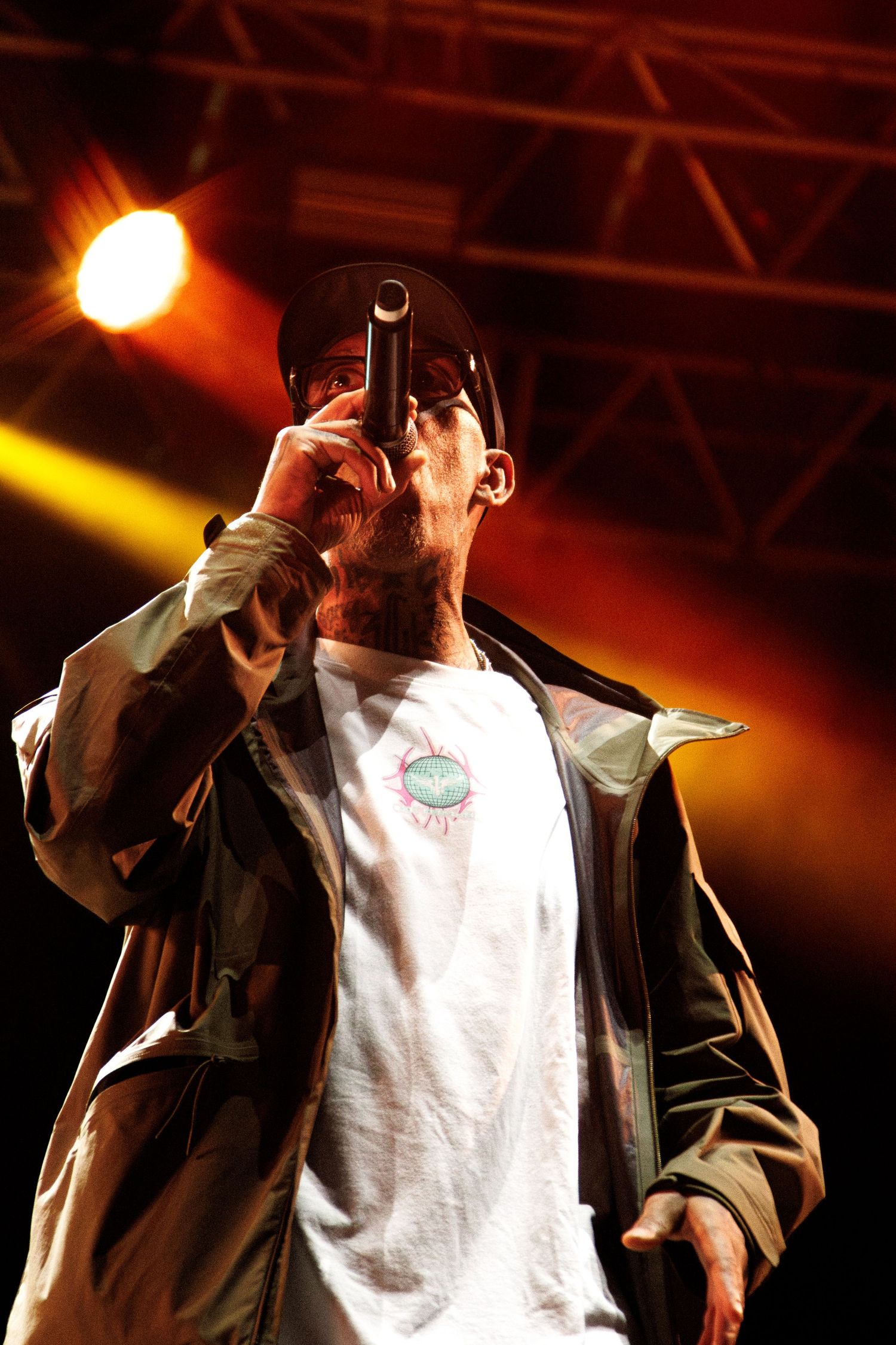 Concert performer in dark jacket and white shirt sings emotively on stage under dramatic orange and yellow lighting.