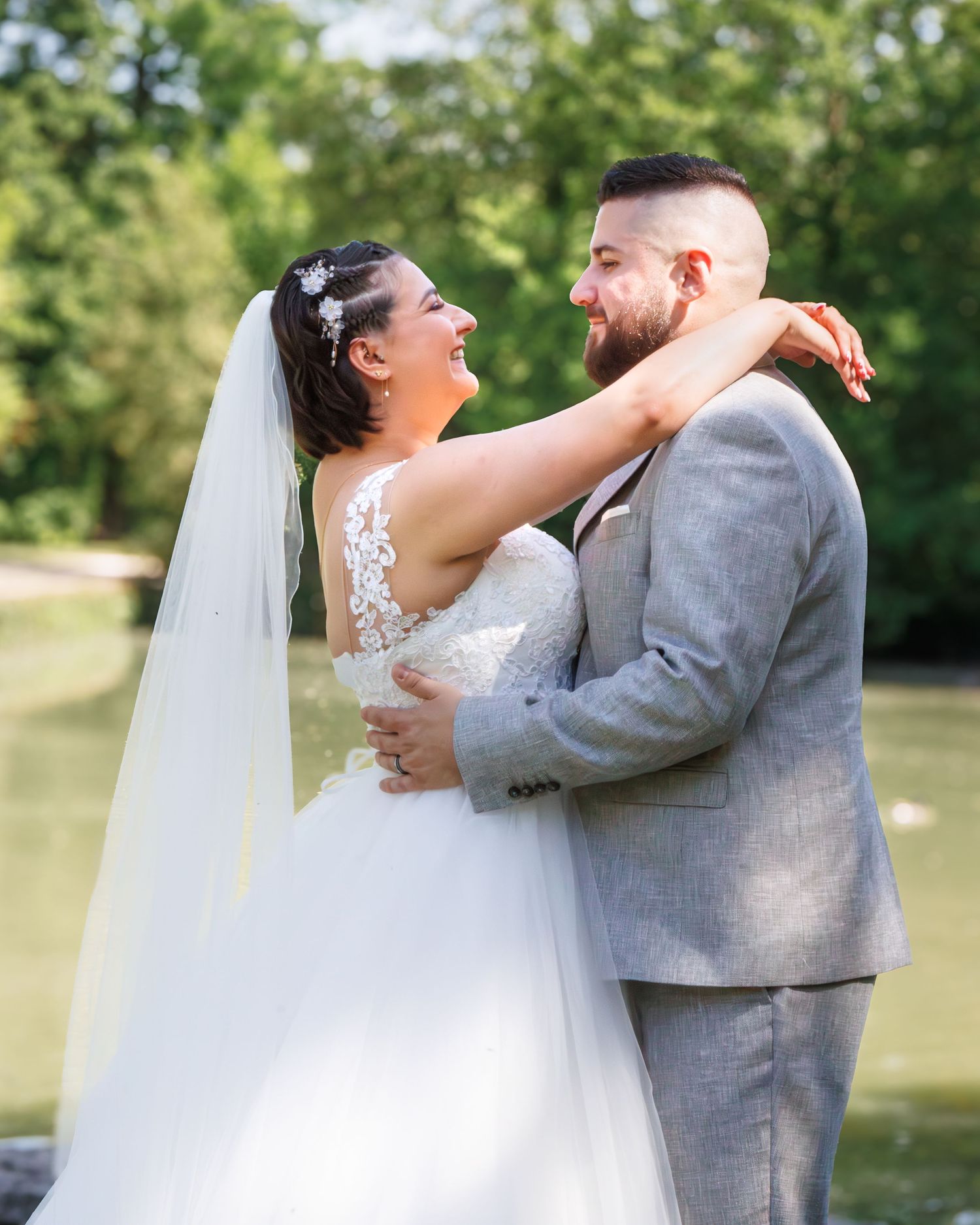 A joyful wedding couple embraces outdoors in a natural setting with lush greenery in the background.