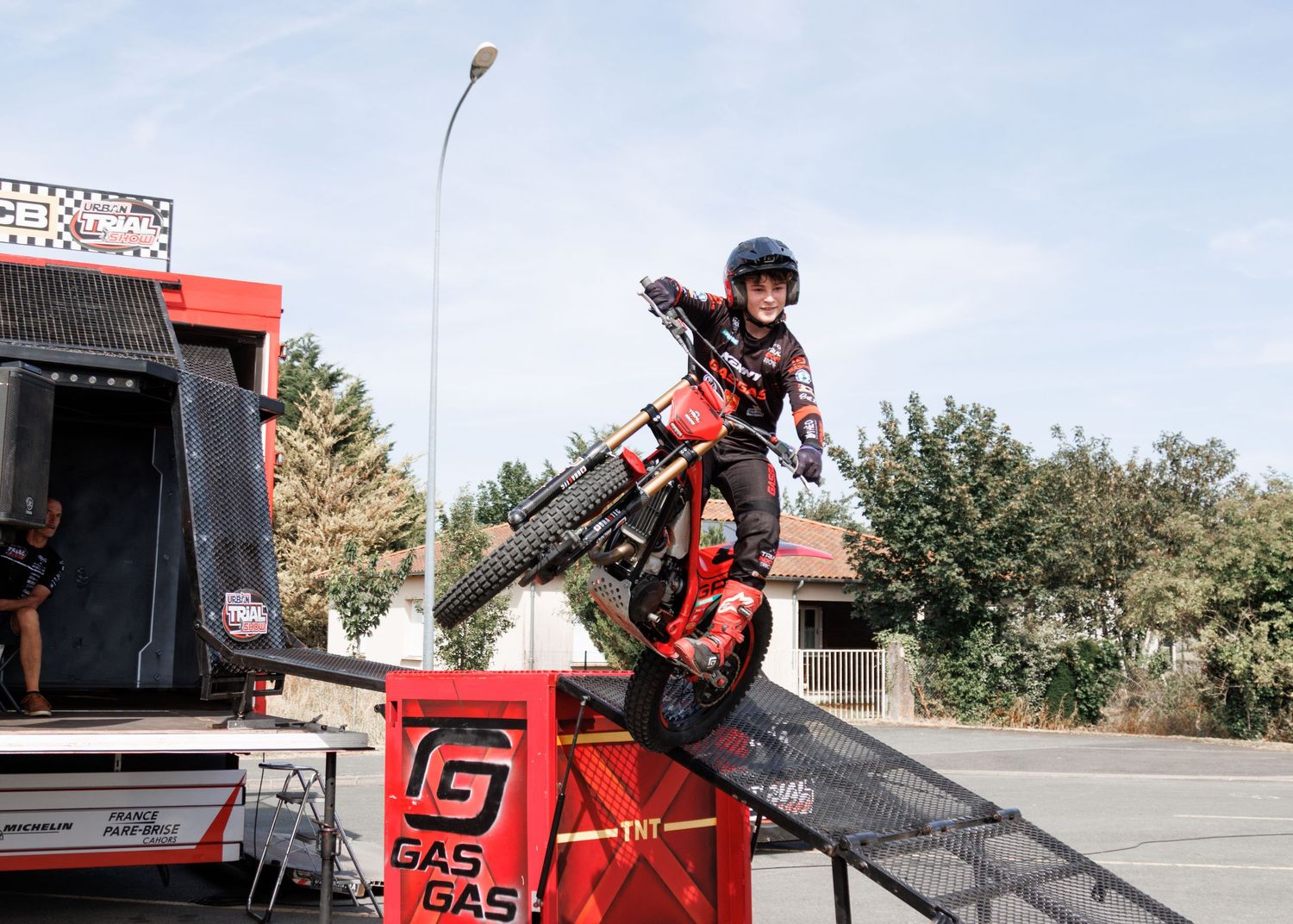 Motocross rider performing a stunt on a GasGas trial bike on a ramp at an outdoor event.