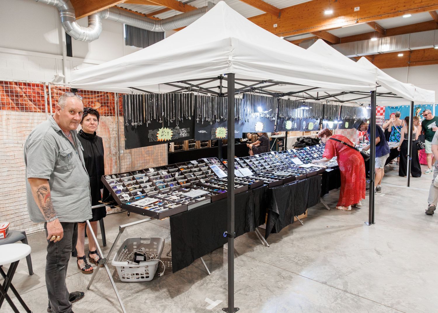 Vendors and shoppers browse a black jewelry display booth at an indoor market fair.