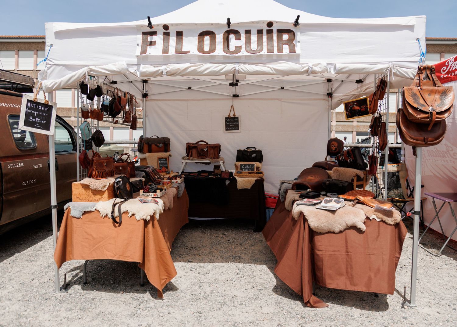 FiloCuir leather goods market stall displaying handcrafted bags and accessories under a white canopy tent.