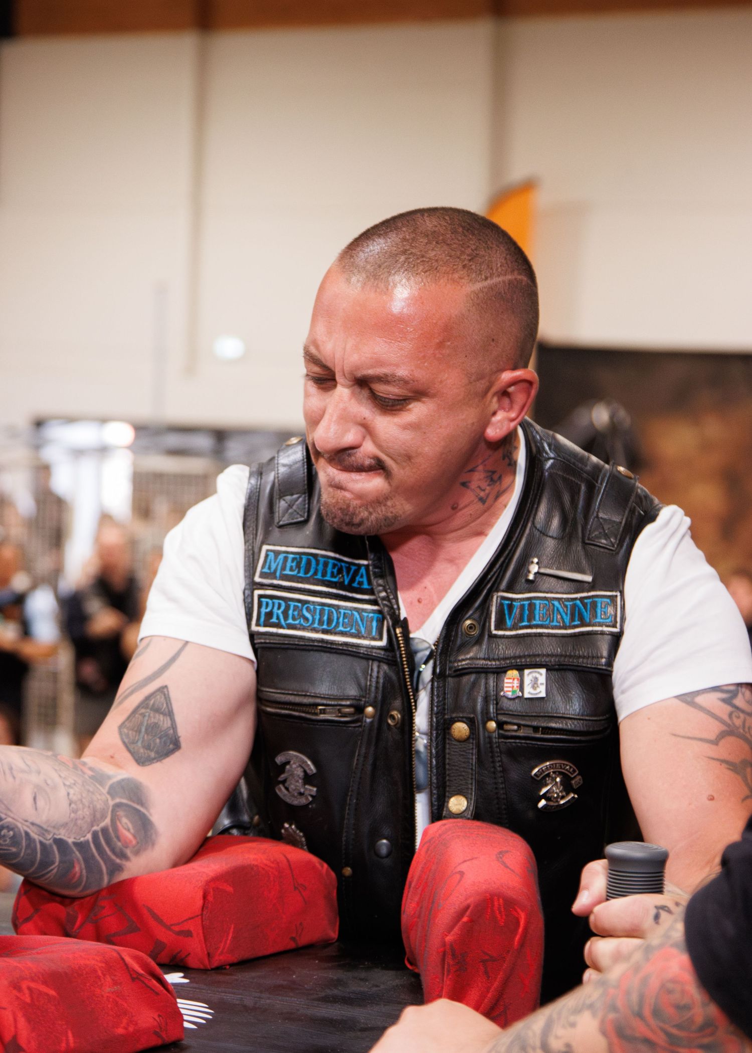 Person in a leather vest with patches demonstrating arm wrestling technique on red pads.