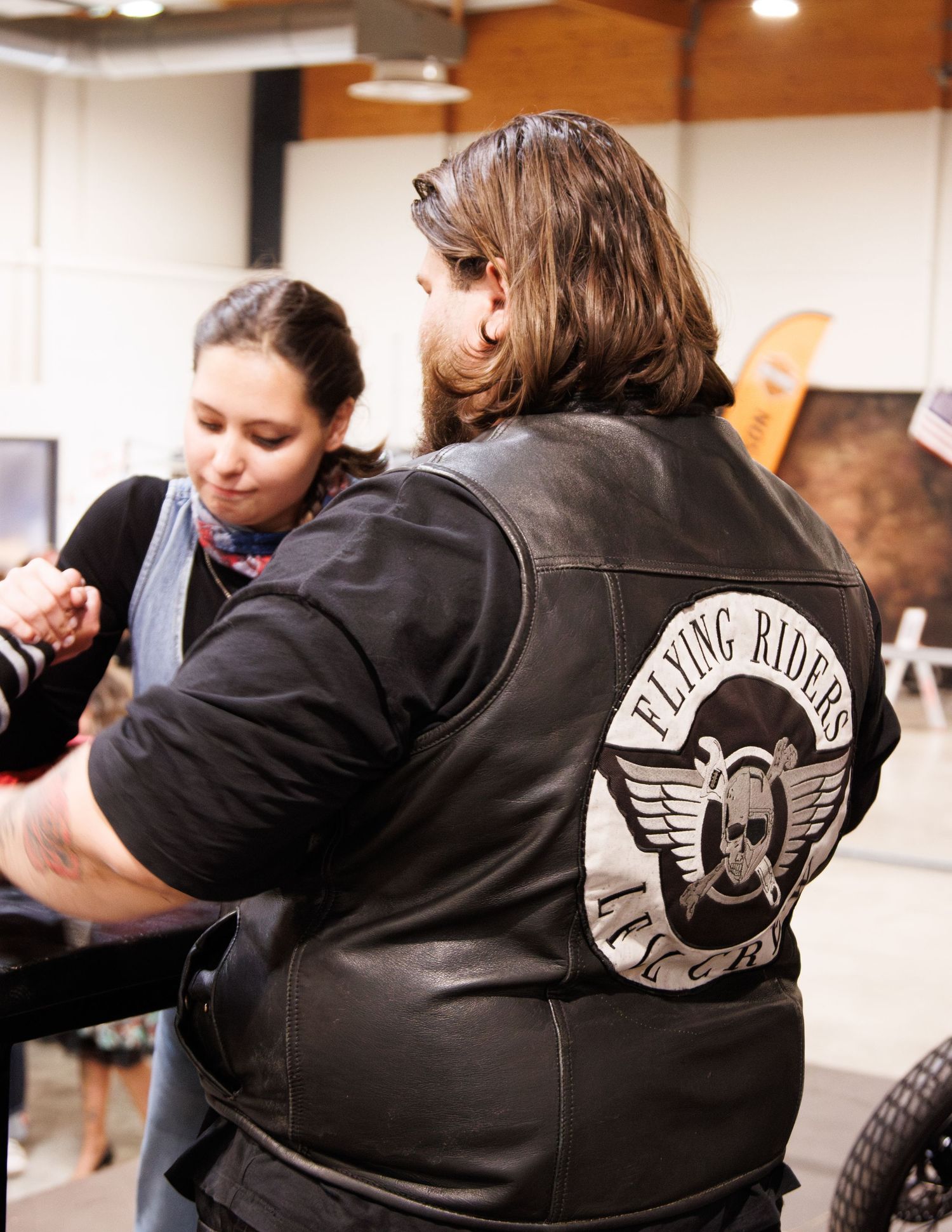 People wearing leather jackets with a riding club patch gather indoors.