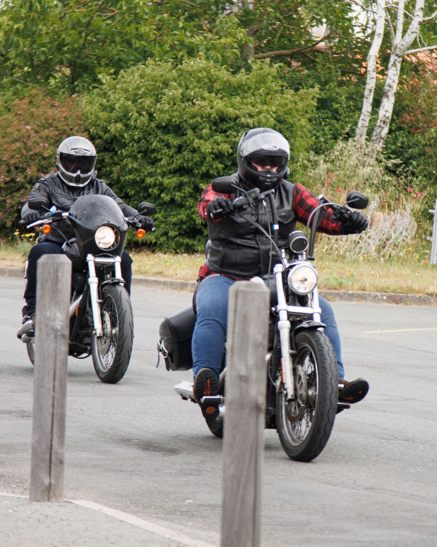 Two motorcyclists riding side by side on street bikes with safety bollards in foreground.