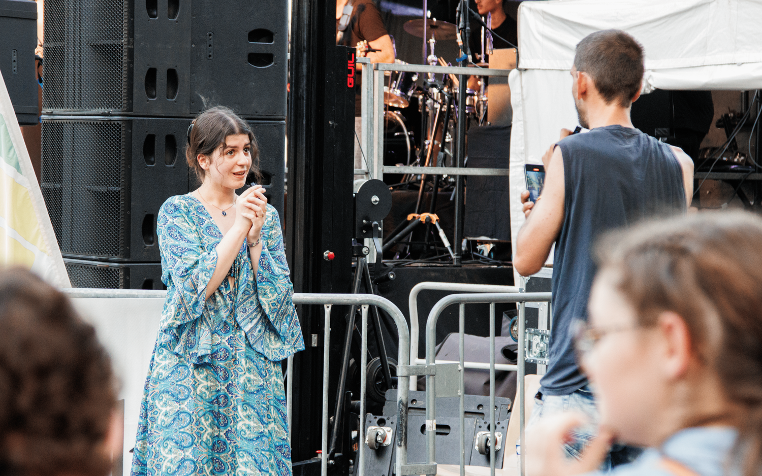 Singer performing at outdoor concert venue with stage equipment visible.