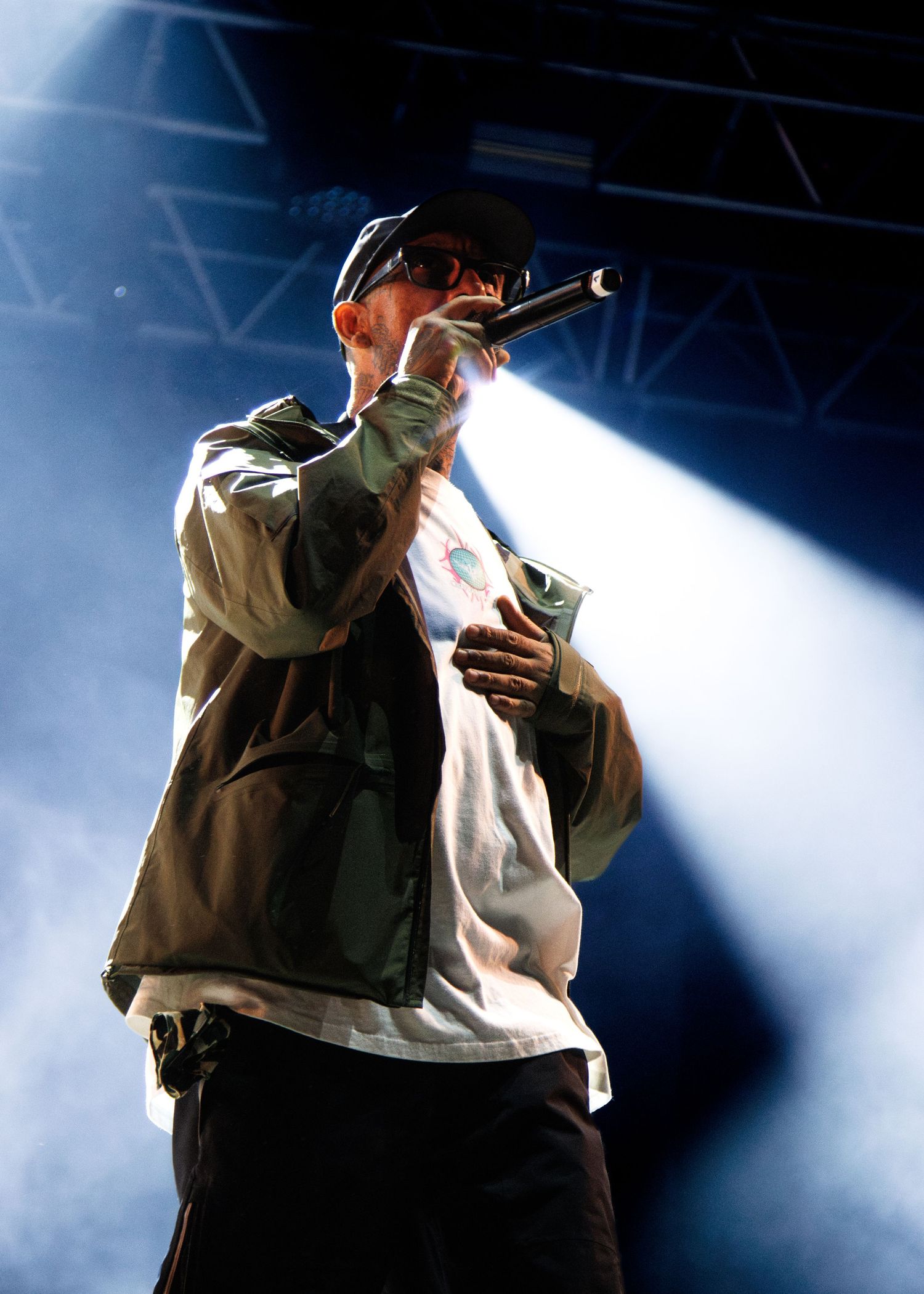 A performer in brown jacket and white shirt sings on stage with dramatic blue spotlights creating an atmospheric backdrop.