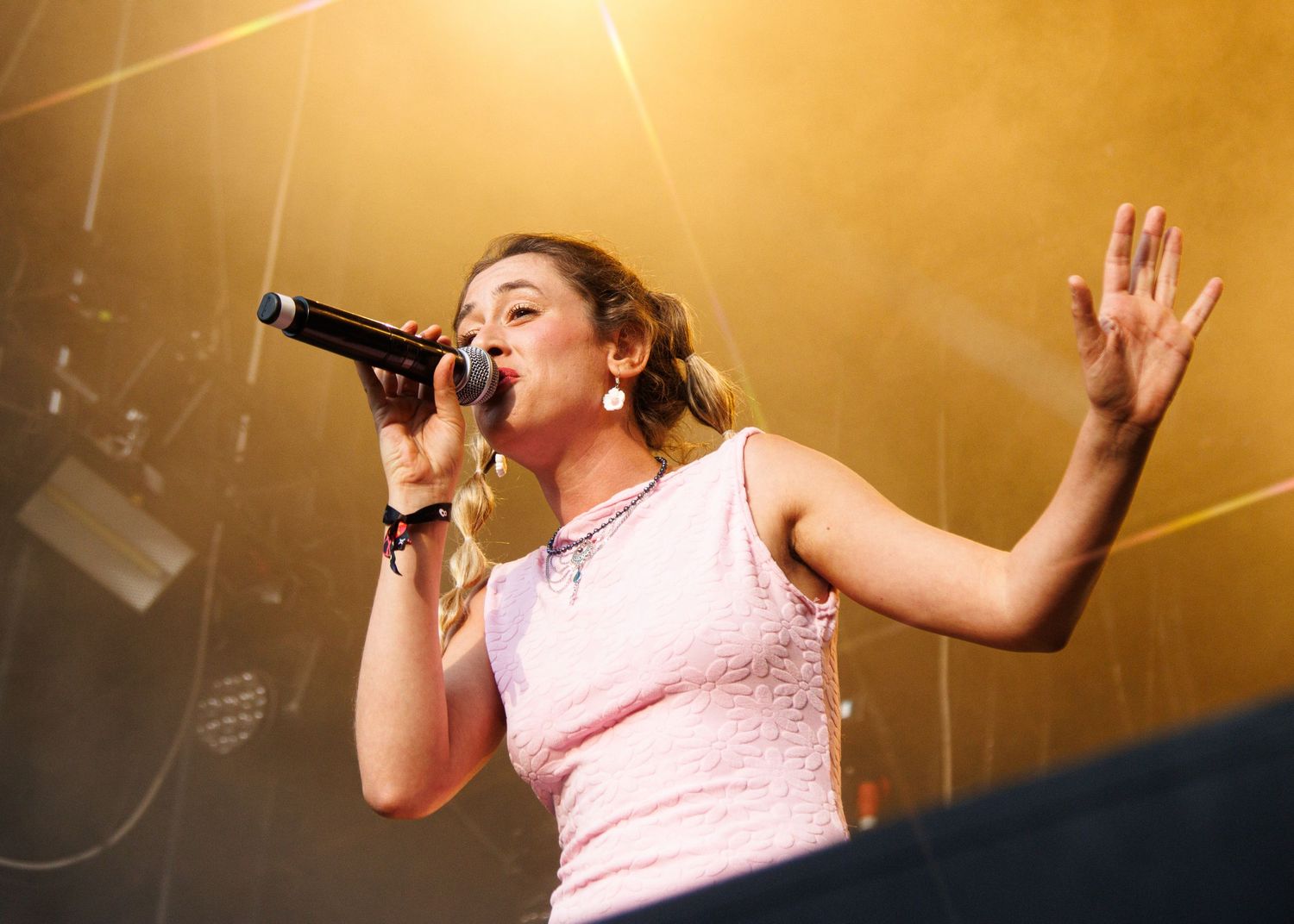 A performer in a pink top sings passionately on stage under warm golden lighting.