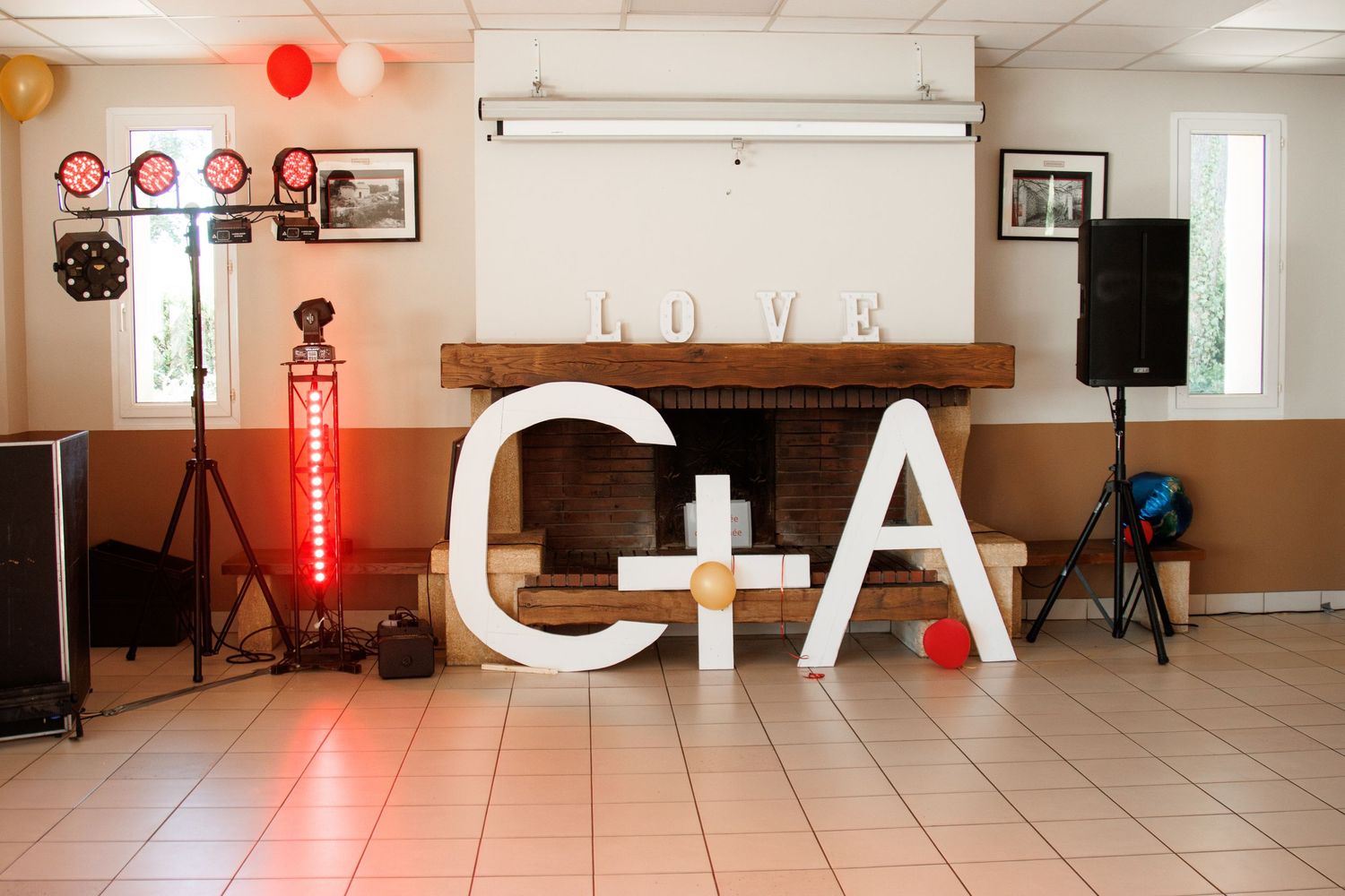 Wedding reception hall decorated with large white C+A letter signs, LOVE marquee letters above fireplace with colorful balloons.
