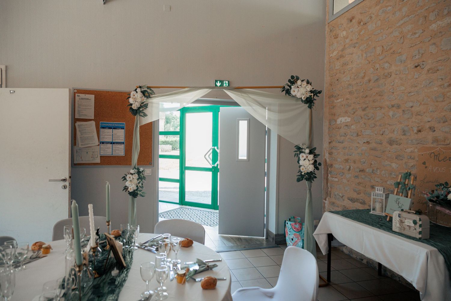 Wedding venue interior decorated with white floral arch over green door and elegant table settings.