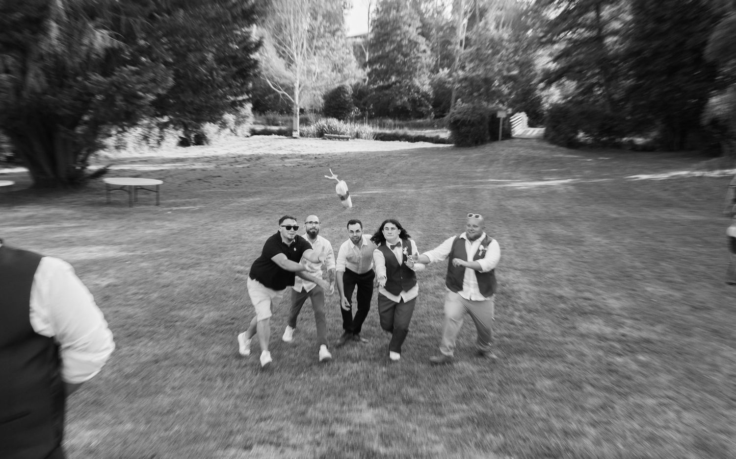 Black and white photo of five wedding guests posing playfully on a green lawn.