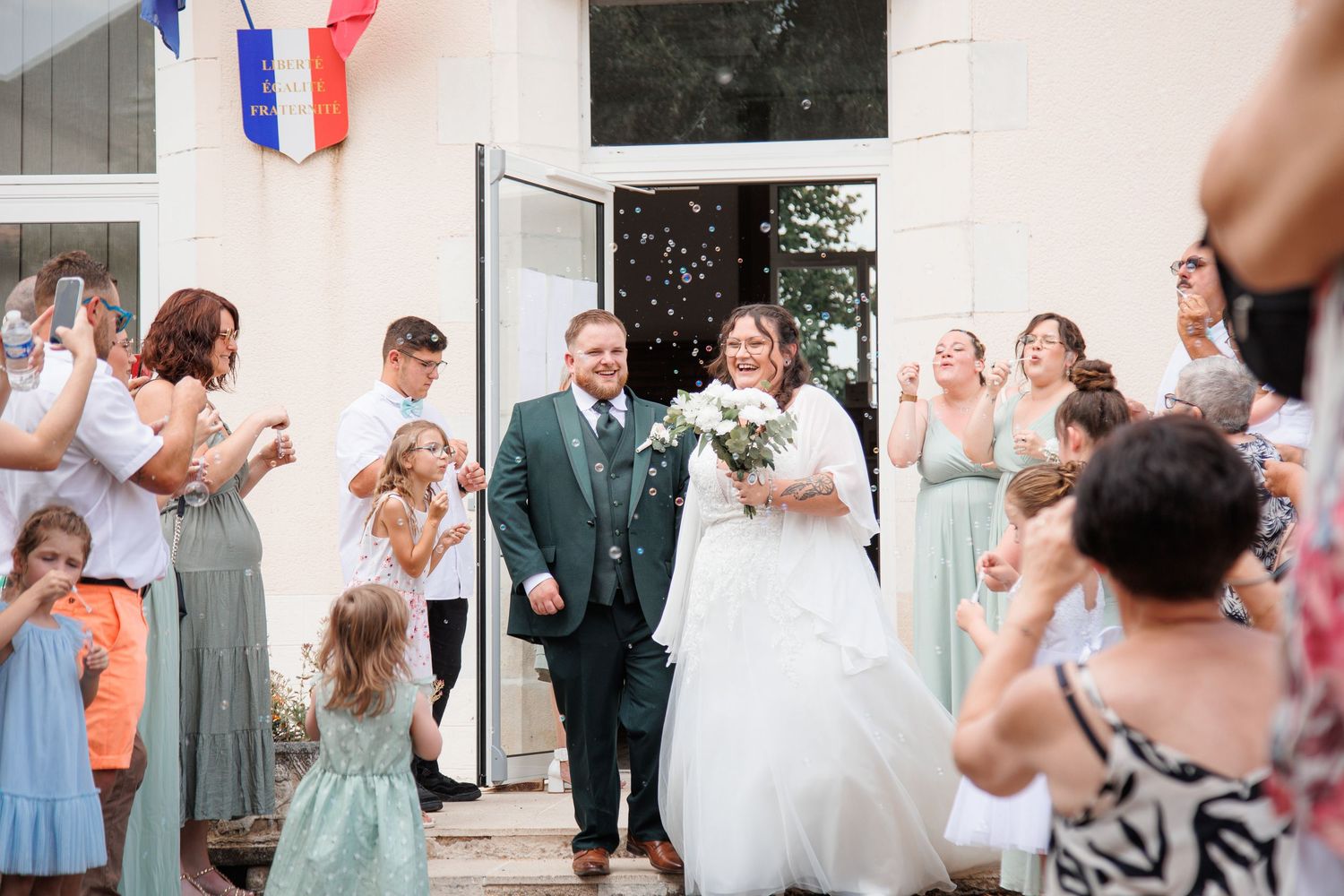 Bride and groom exit wedding venue as guests celebrate with confetti, bridesmaids in sage green dresses lining the path.