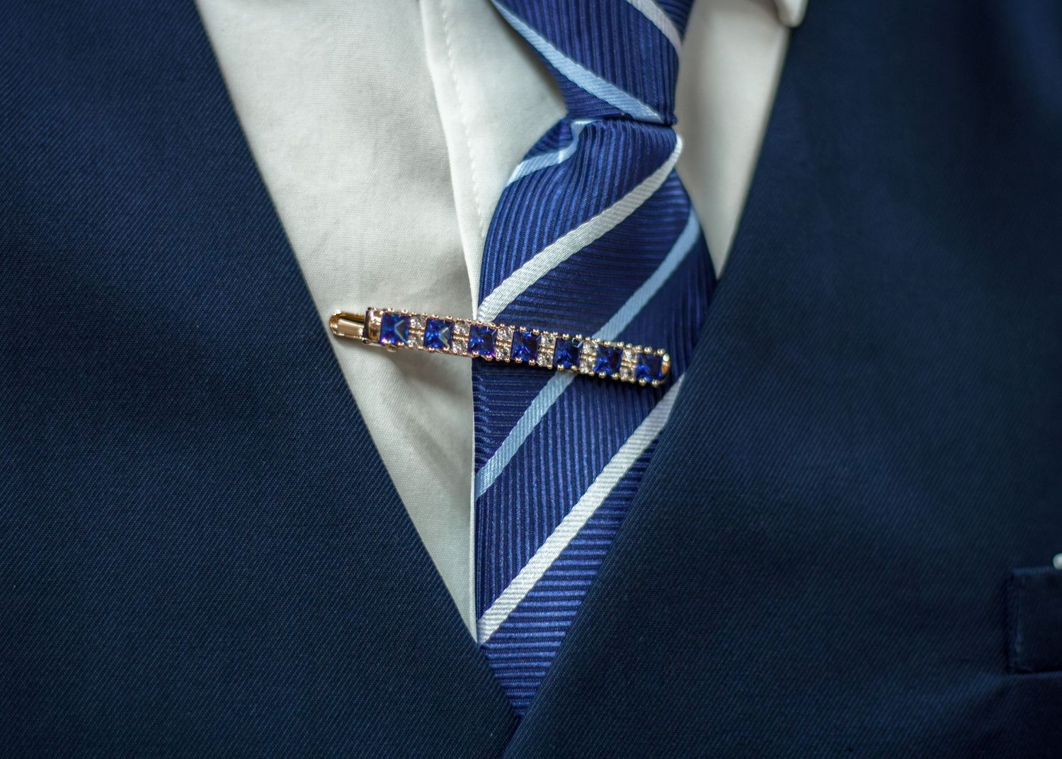 Gold and blue sapphire tie clip on a striped blue tie with navy suit jacket.