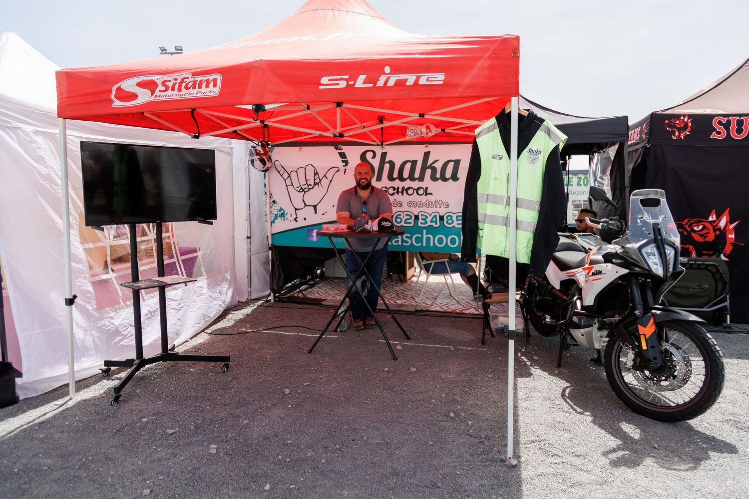 Shaka school event booth with Sifam and S-Line branding, featuring a performer, speakers, and a motorcycle on display.
