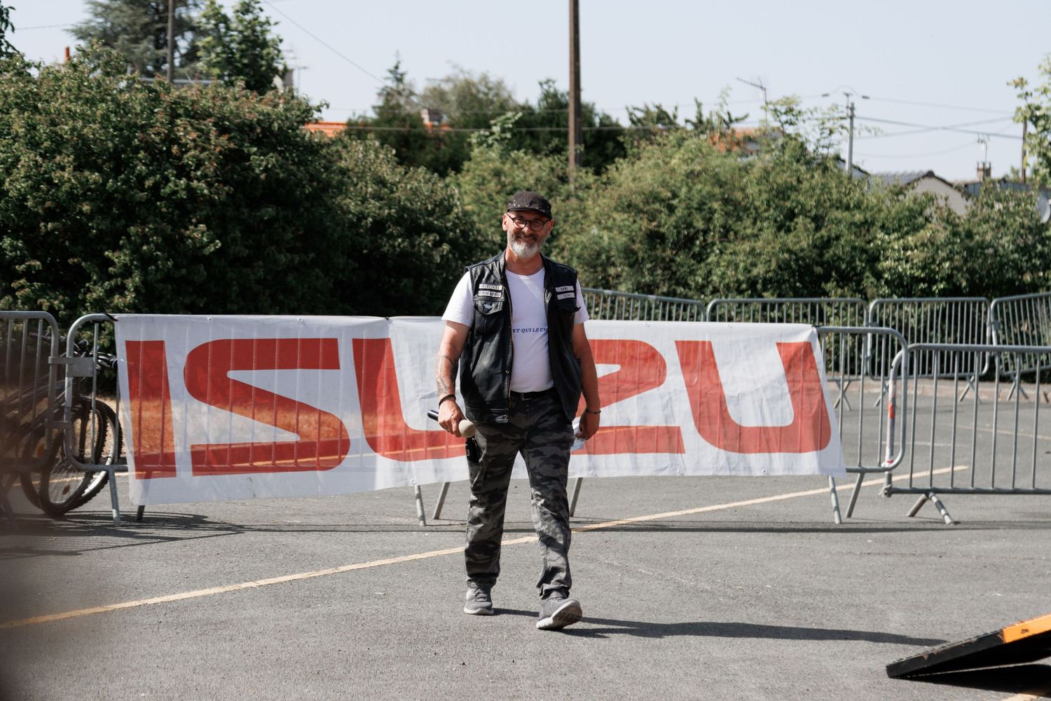 Man walking in front of an Isuzu banner at an outdoor event on a sunny day.