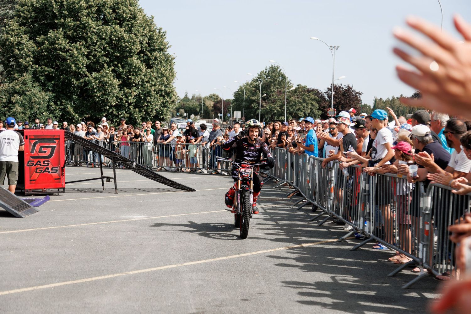 Motocross rider performs stunt on ramp before large crowd at outdoor GasGas motorcycle event on sunny day.