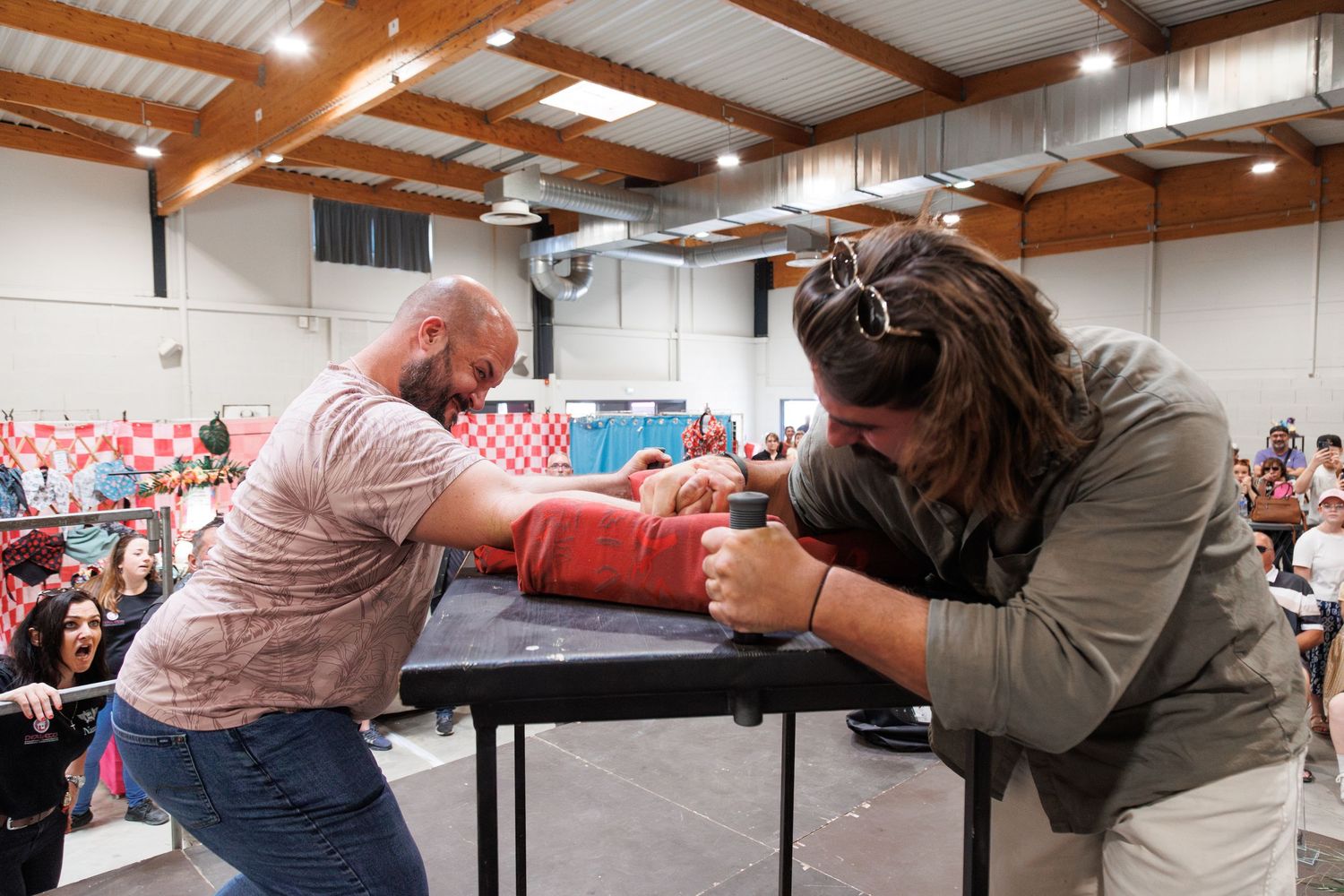 Two competitors engage in an intense arm wrestling match on a black table before a large crowd at an indoor event.