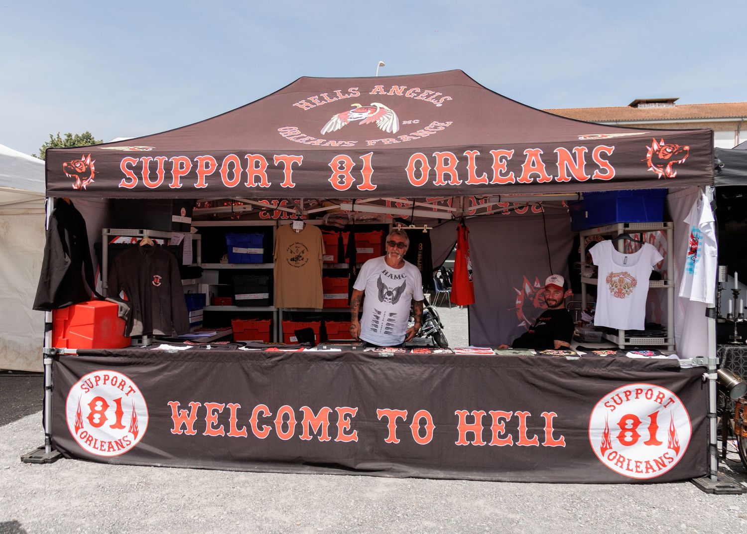 Hells Angels Support 81 Orleans merchandise booth with Welcome to Hell banner at outdoor event.