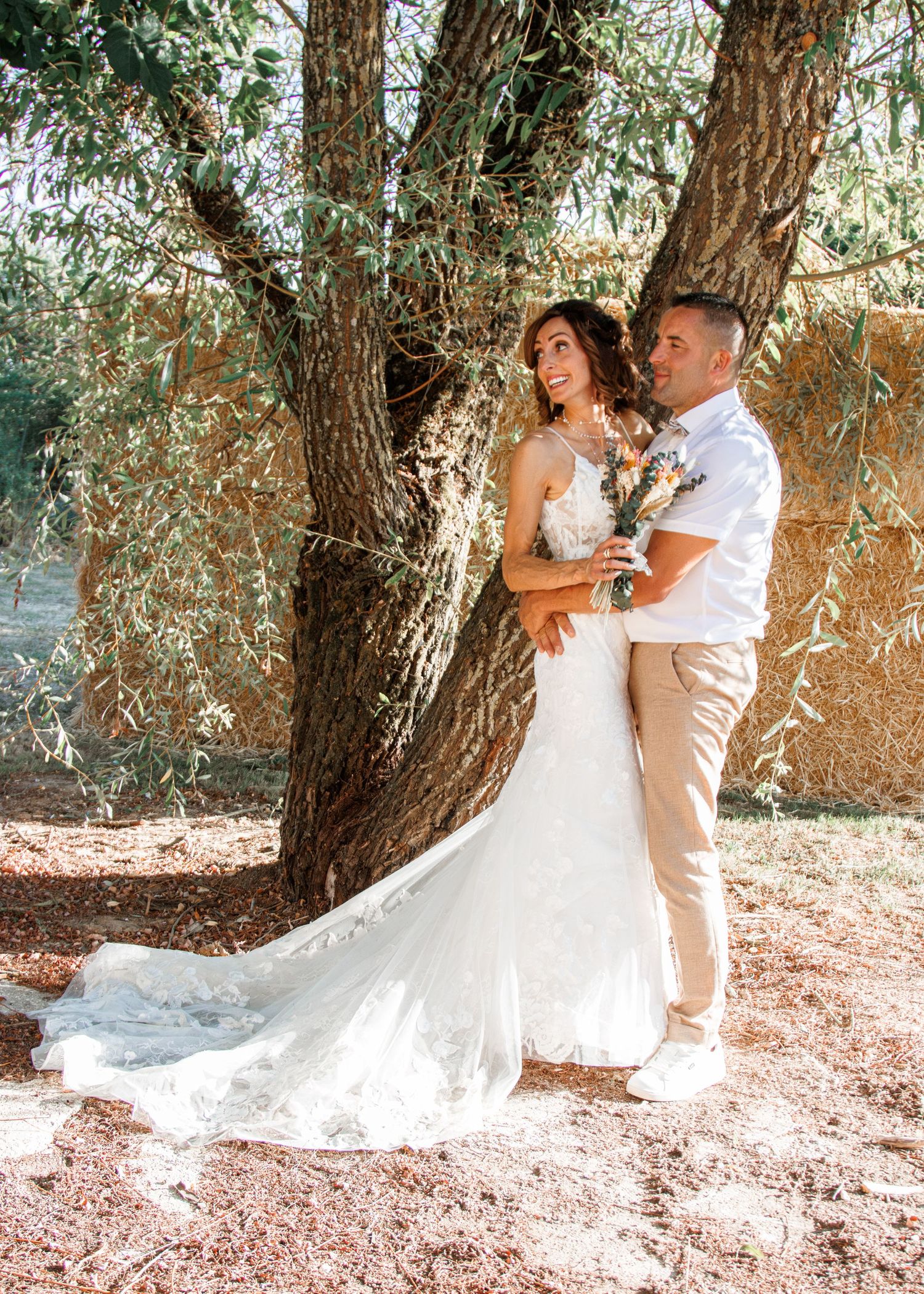 A romantic couple in white attire share intimate moments under a tree in a series of outdoor wedding photographs.