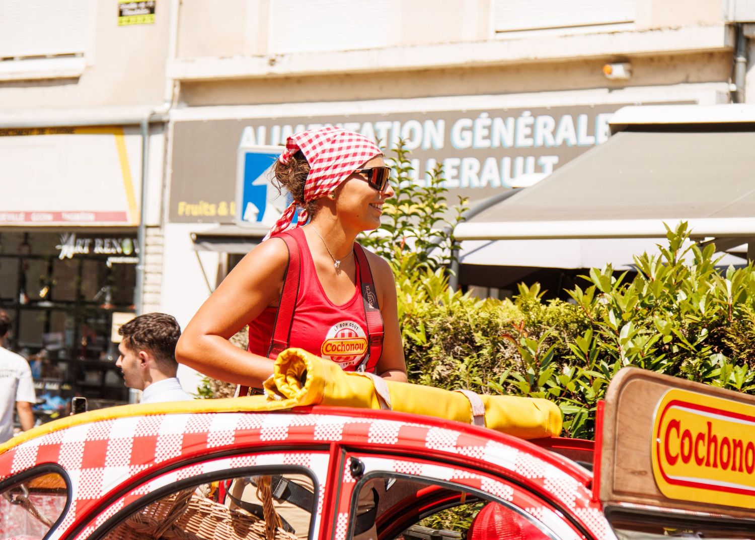 Decorated vintage car with red checkered pattern participates in street parade while spectators watch.
