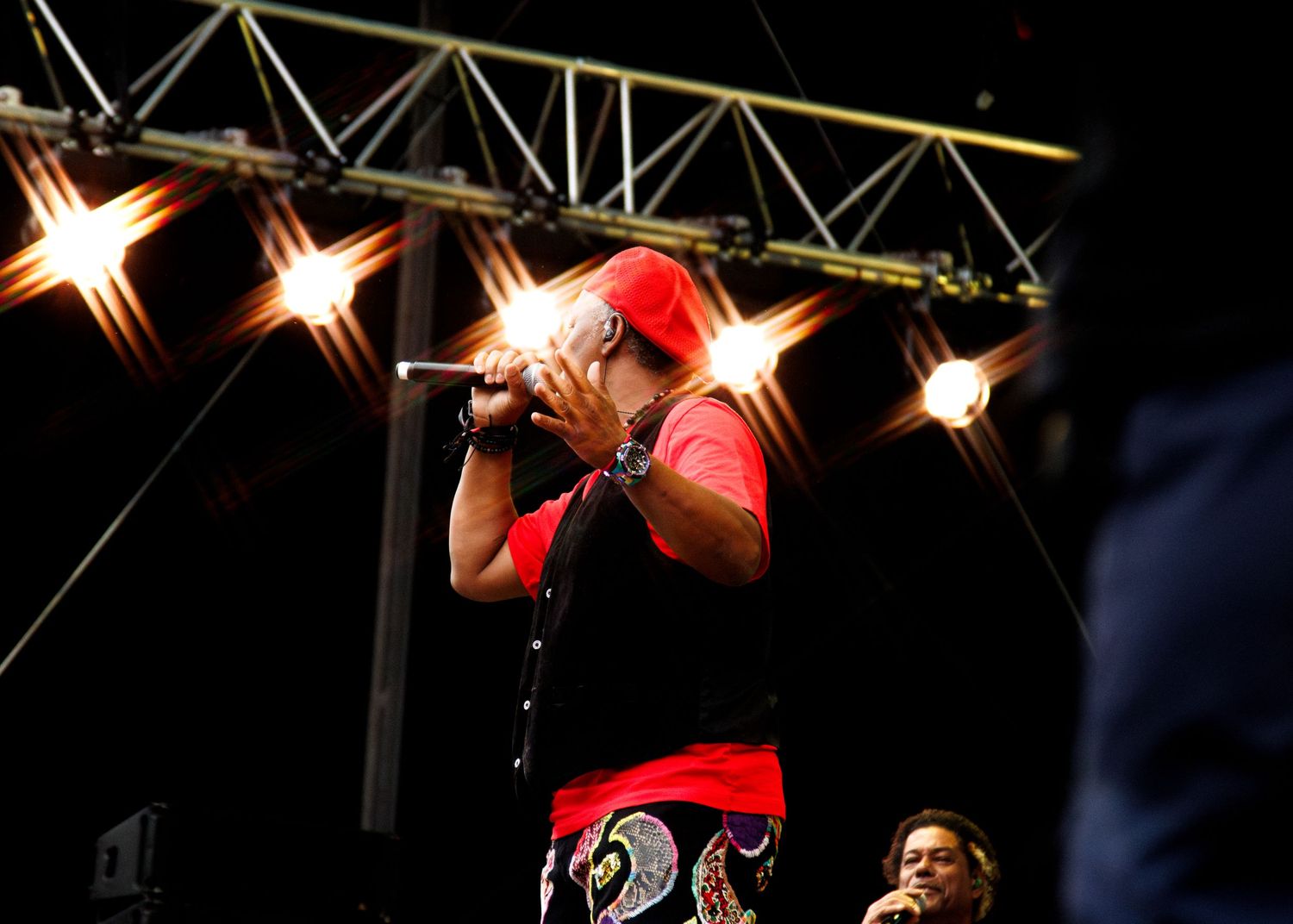 Performer in bright red outfit energetically singing on stage under dramatic spotlights.