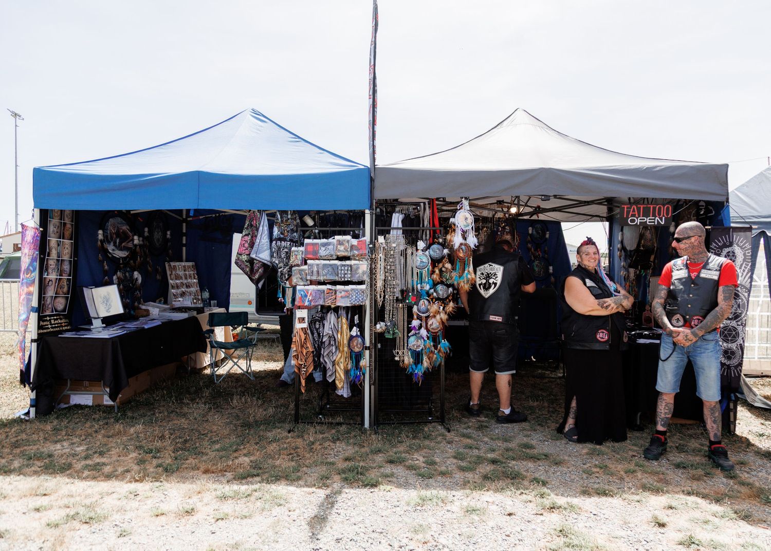 Outdoor market stalls with blue and black canopy tents displaying jewelry and merchandise at a summer festival.