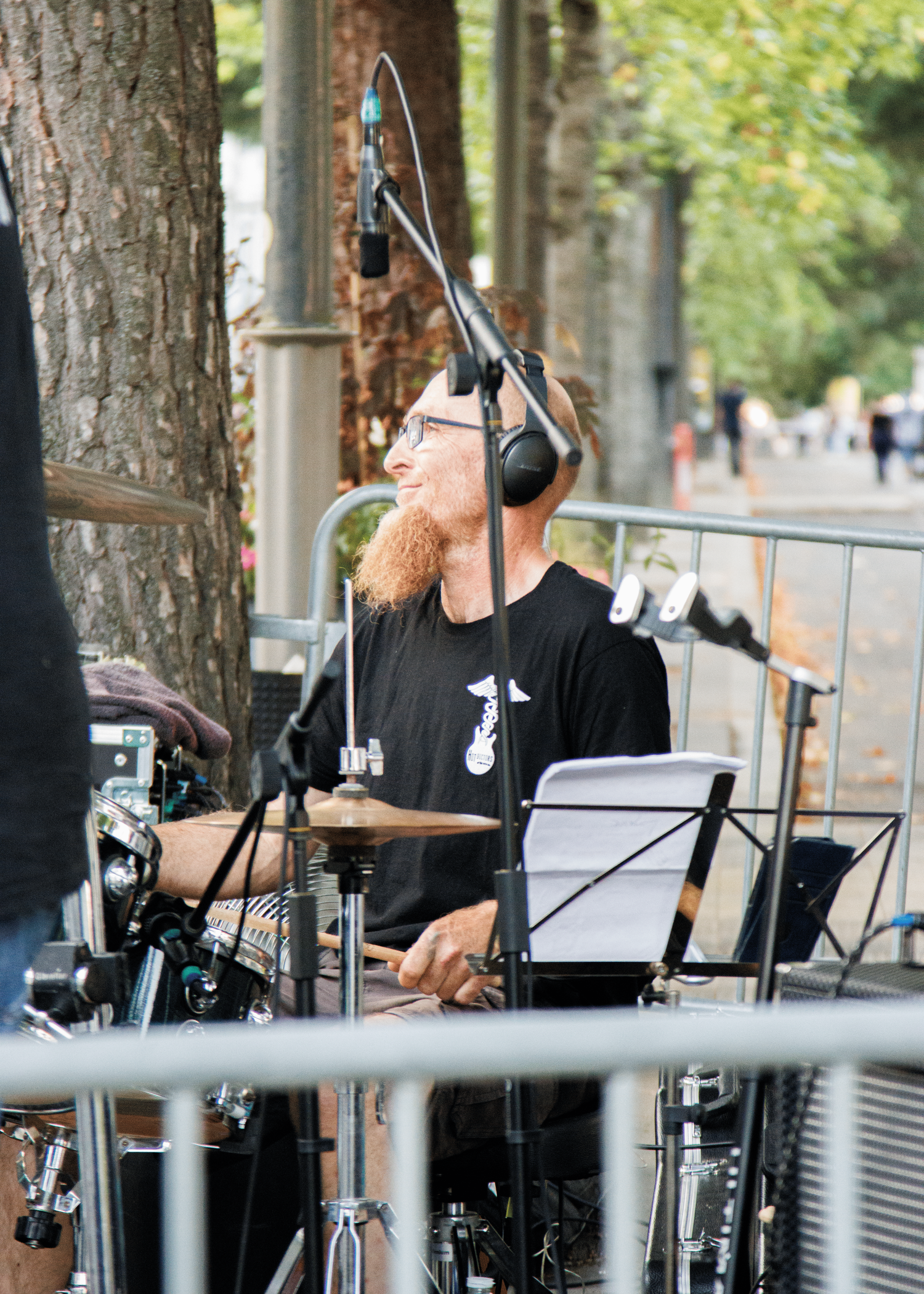 Drummer wearing headphones performs behind drumkit at outdoor concert.