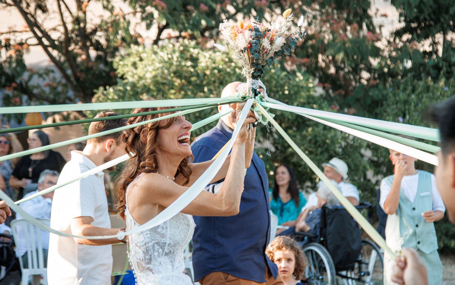 A happy couple celebrates their wedding ceremony under outdoor decorative ribbons and streamers in a garden setting.
