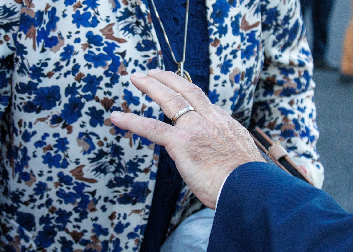 Close-up of an elderly person's hand with a silver ring resting on a floral blue and white jacket.