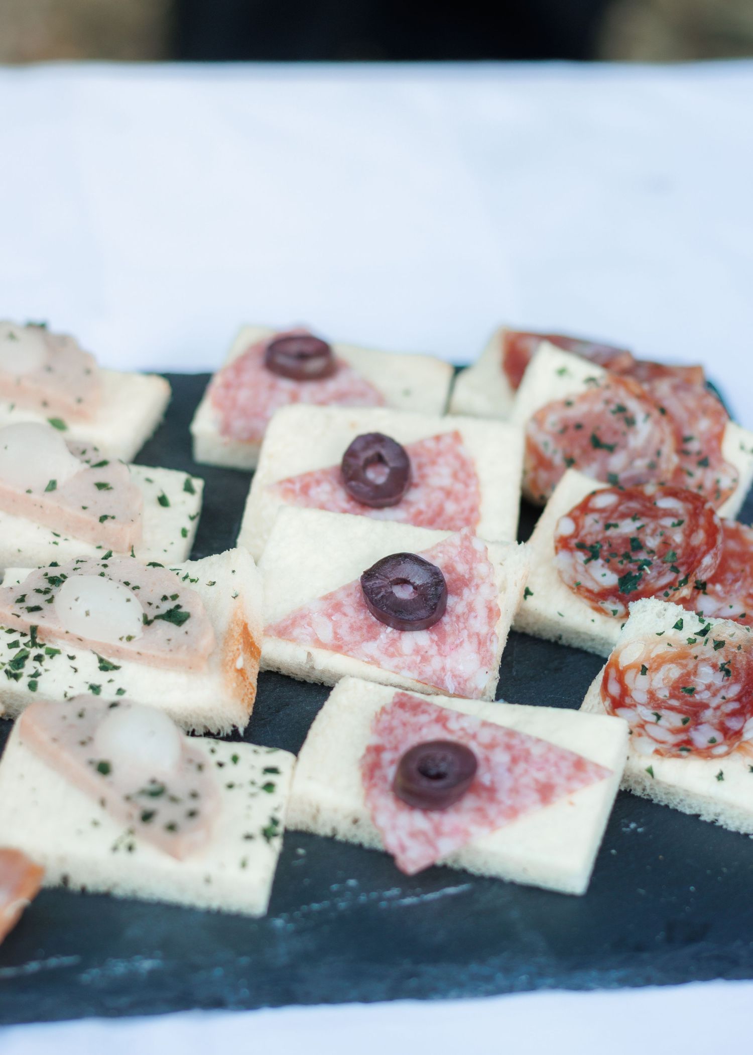 Elegant appetizers on slate board featuring salami, cheese and olive canapes at a wedding reception.