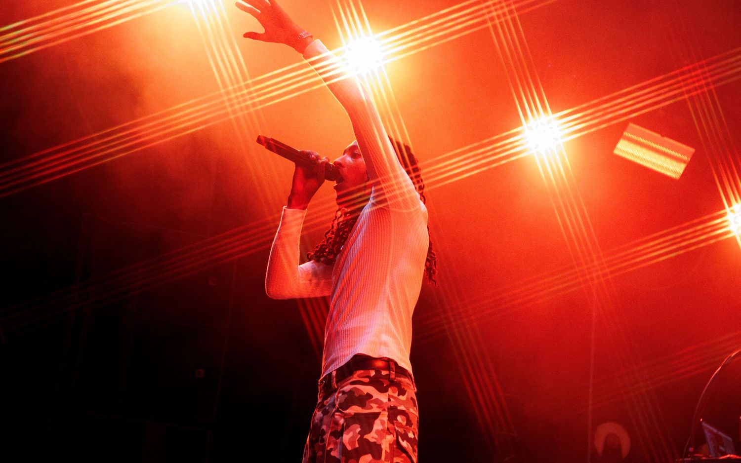 A performer raises their arm dramatically on stage bathed in red light with bright spotlights behind them.