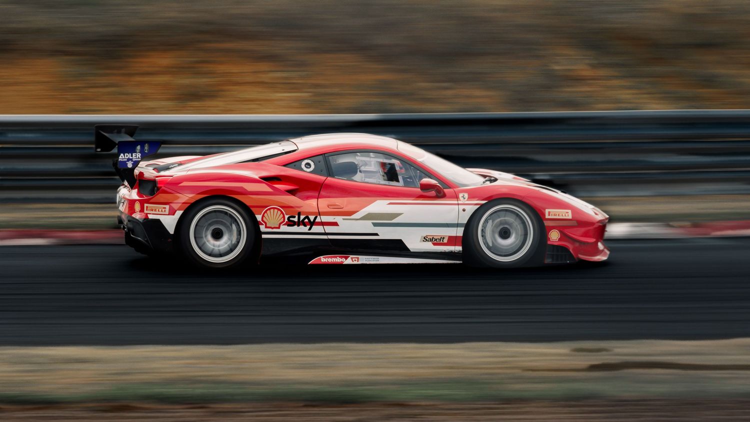 Red racing Ferrari zooms past on track with dramatic motion blur effect.