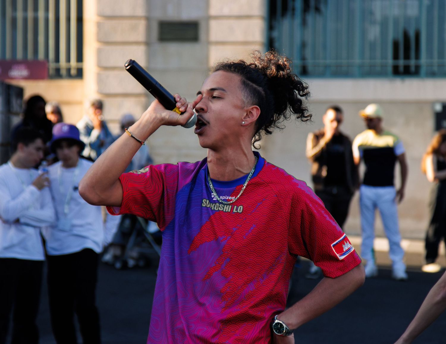 Performer in red and purple shirt energetically singing into microphone at outdoor venue.