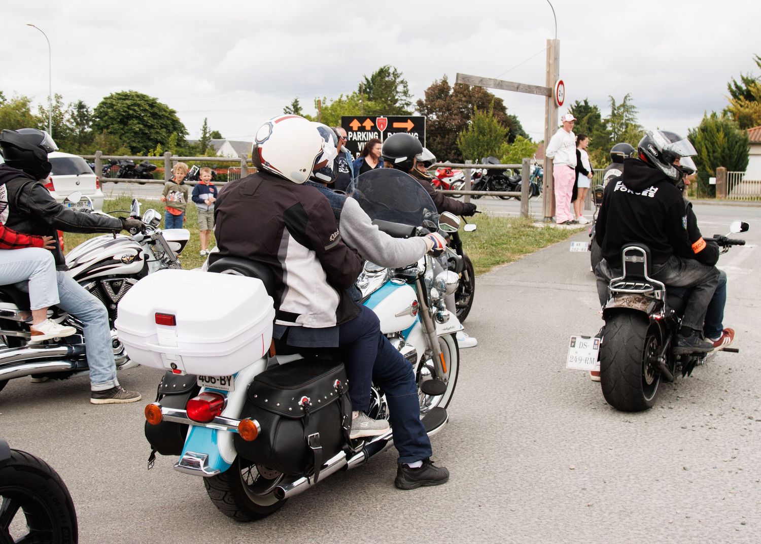 Group of motorcyclists in protective gear gathered on street with parked bikes.