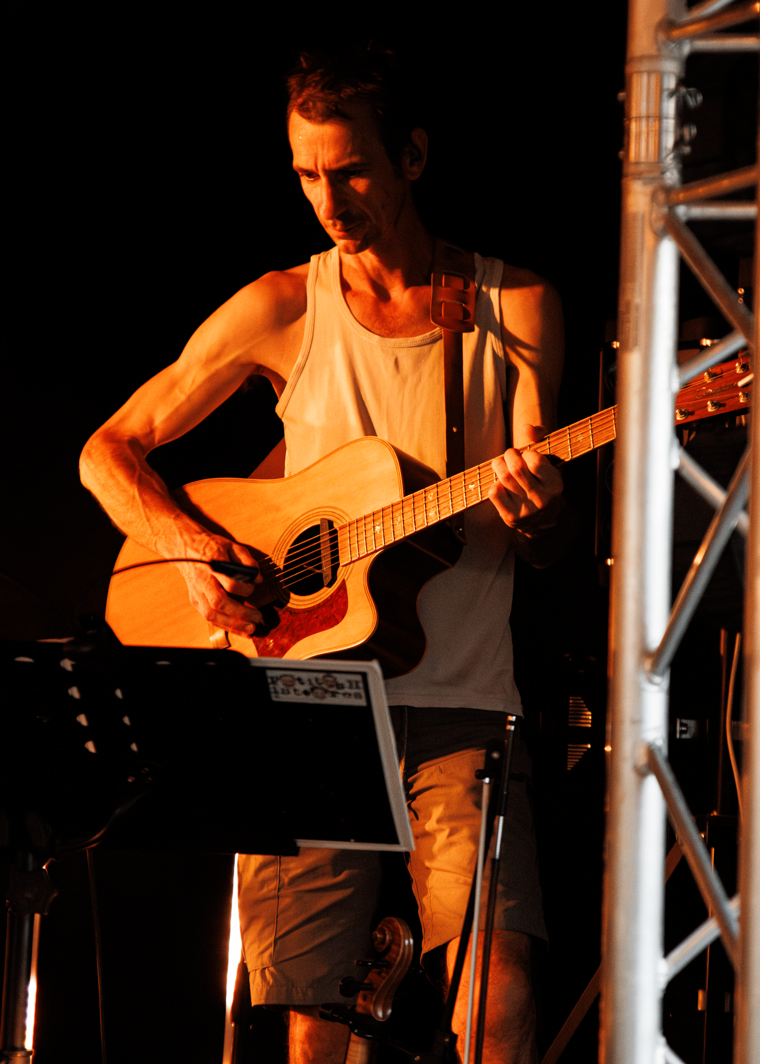 Musician playing acoustic guitar under dramatic orange stage lighting.