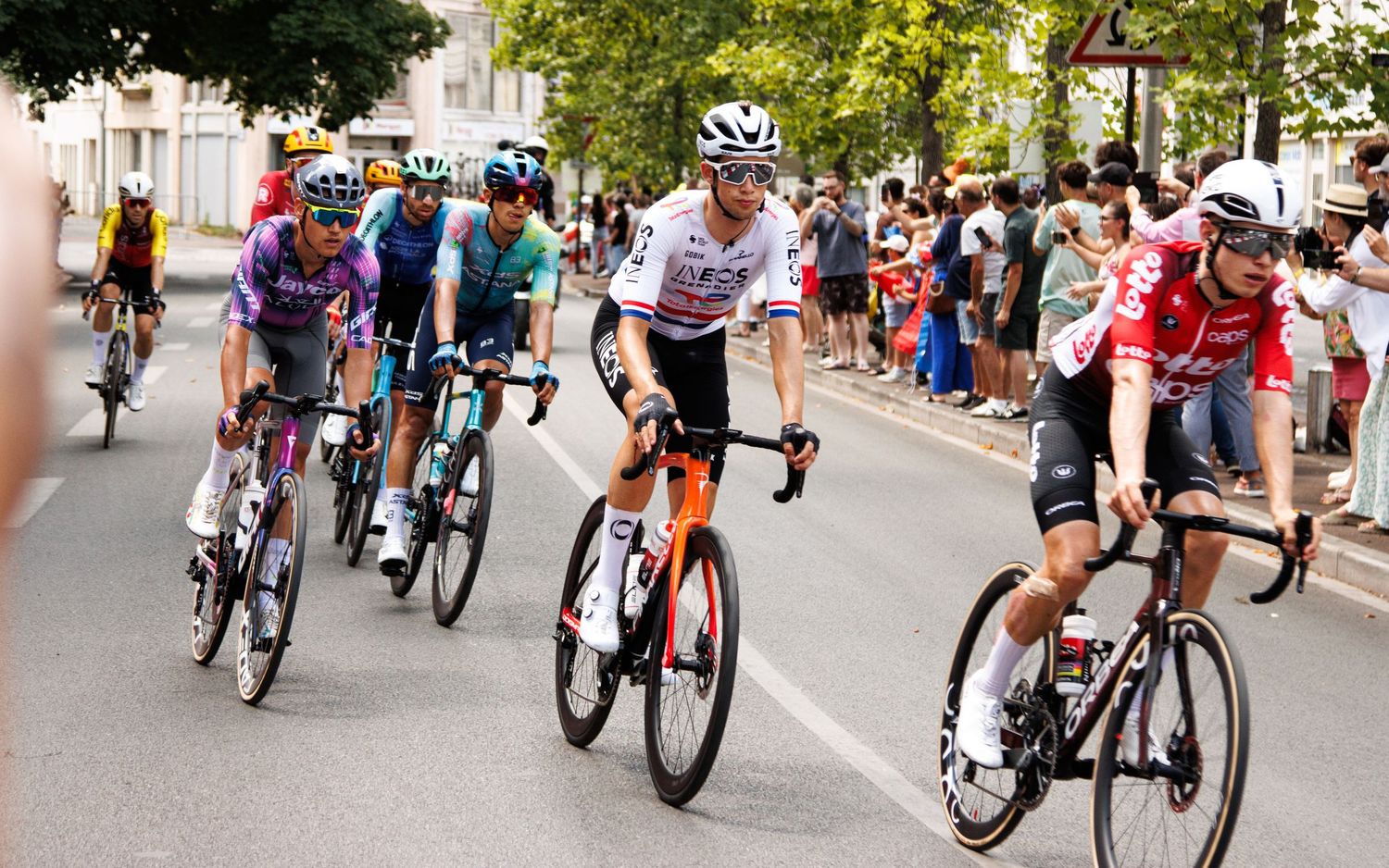 Professional cyclists race through city streets during a competitive cycling event with crowds watching.