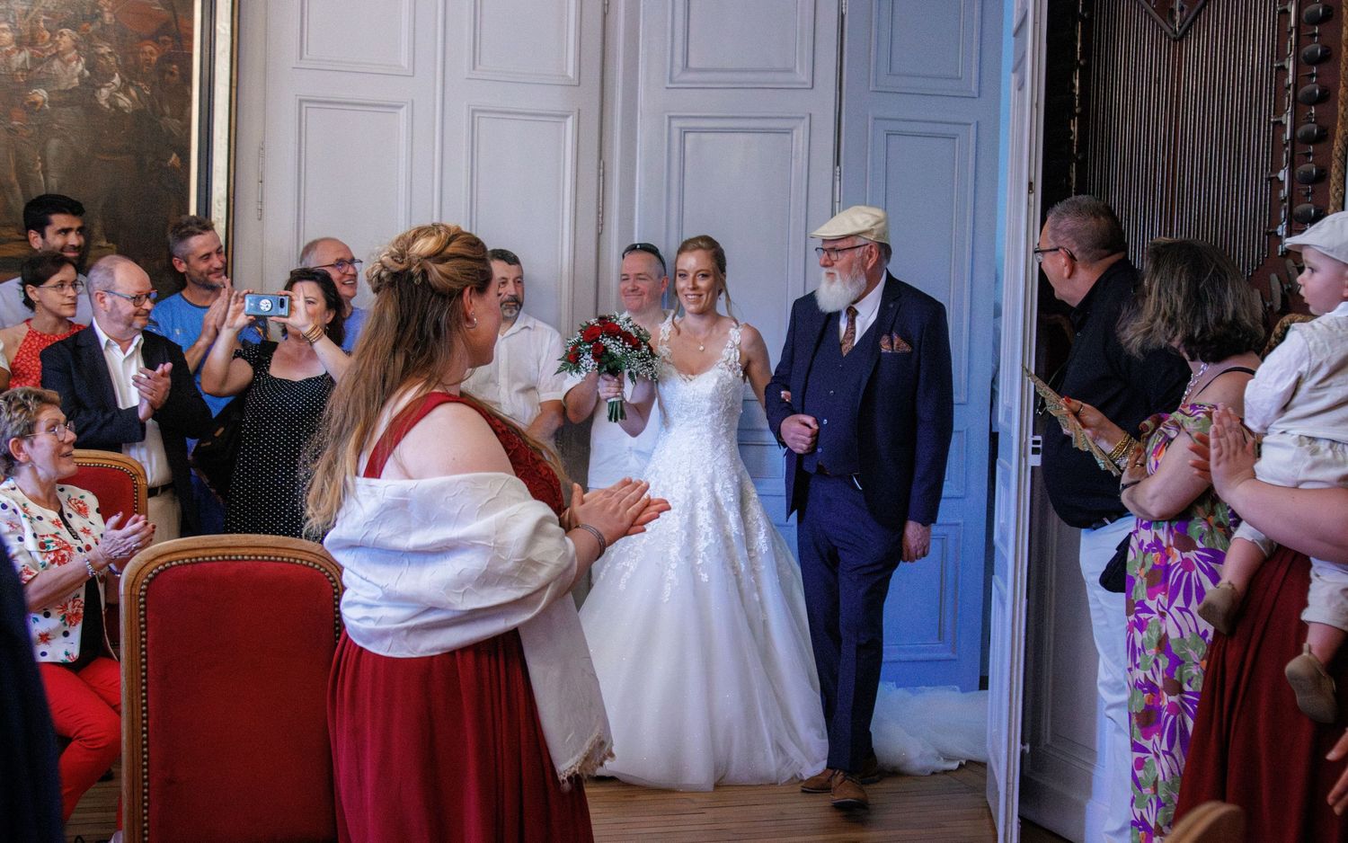 Bride and groom walk down the aisle as guests celebrate in a grand ceremonial room.