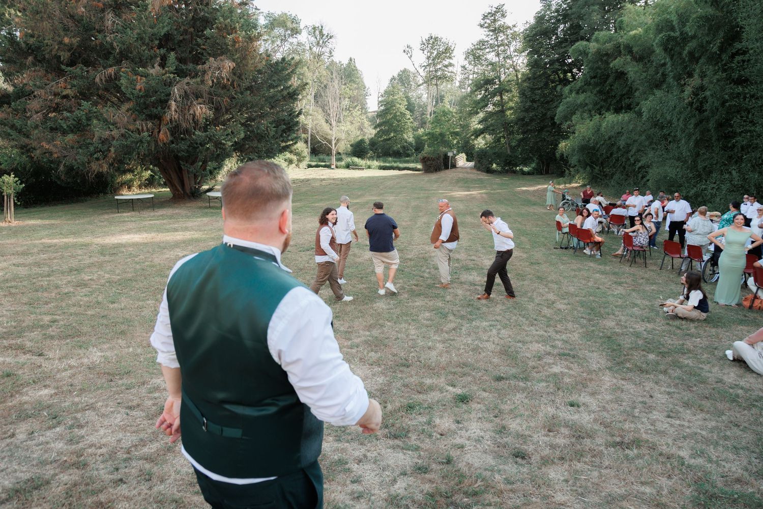 Wedding guests playing outdoor lawn games in a lush green park setting.