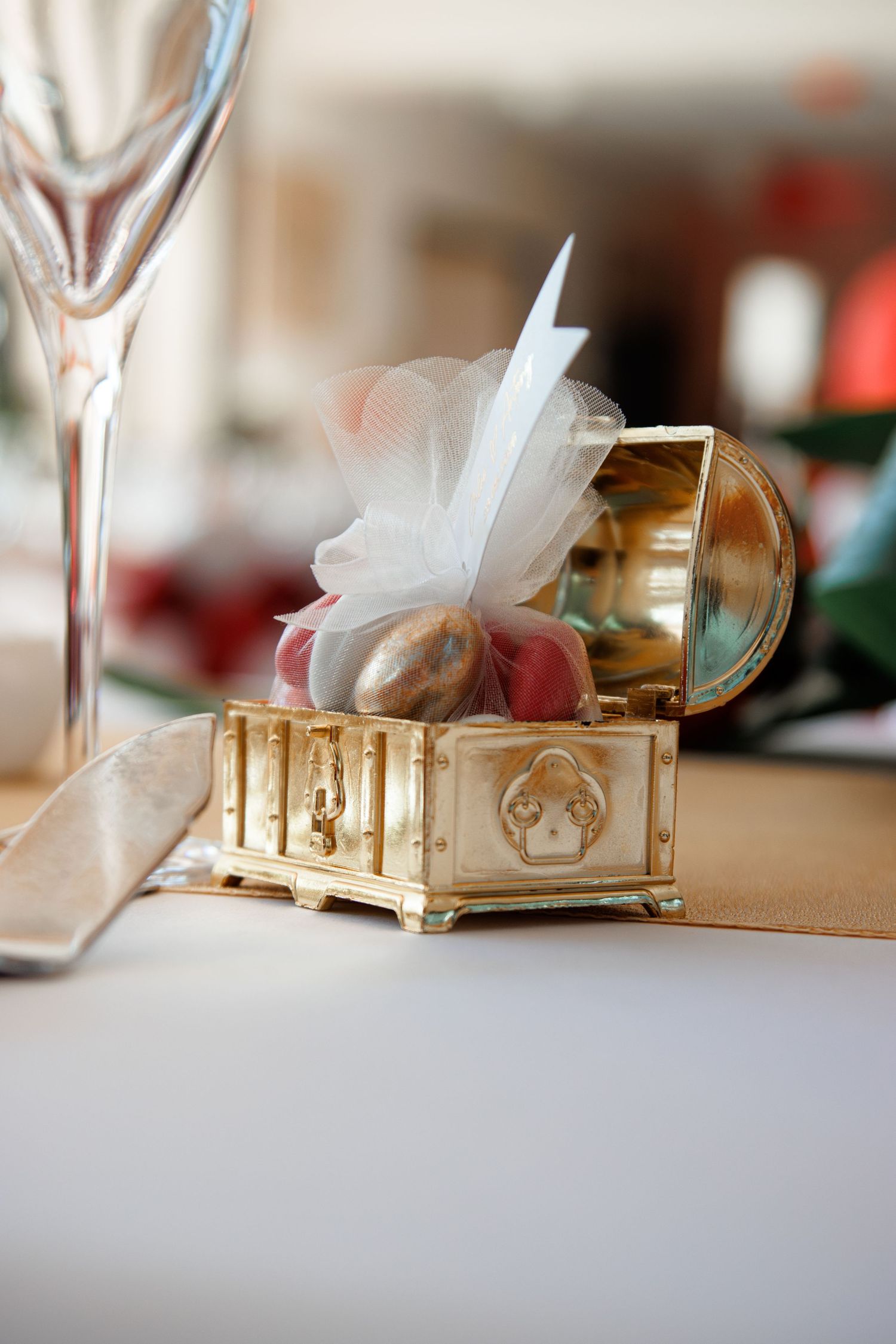 Gold ornate jewelry box with wedding favors wrapped in white tulle ribbon on reception table.