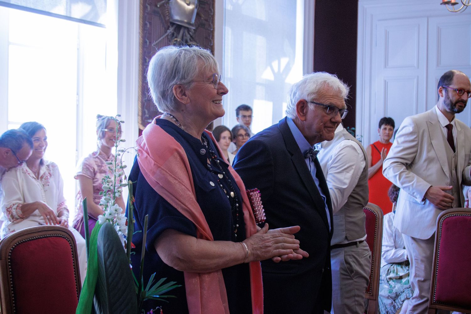 Elegantly dressed elderly couple socializing at a formal wedding reception in a grand hall.