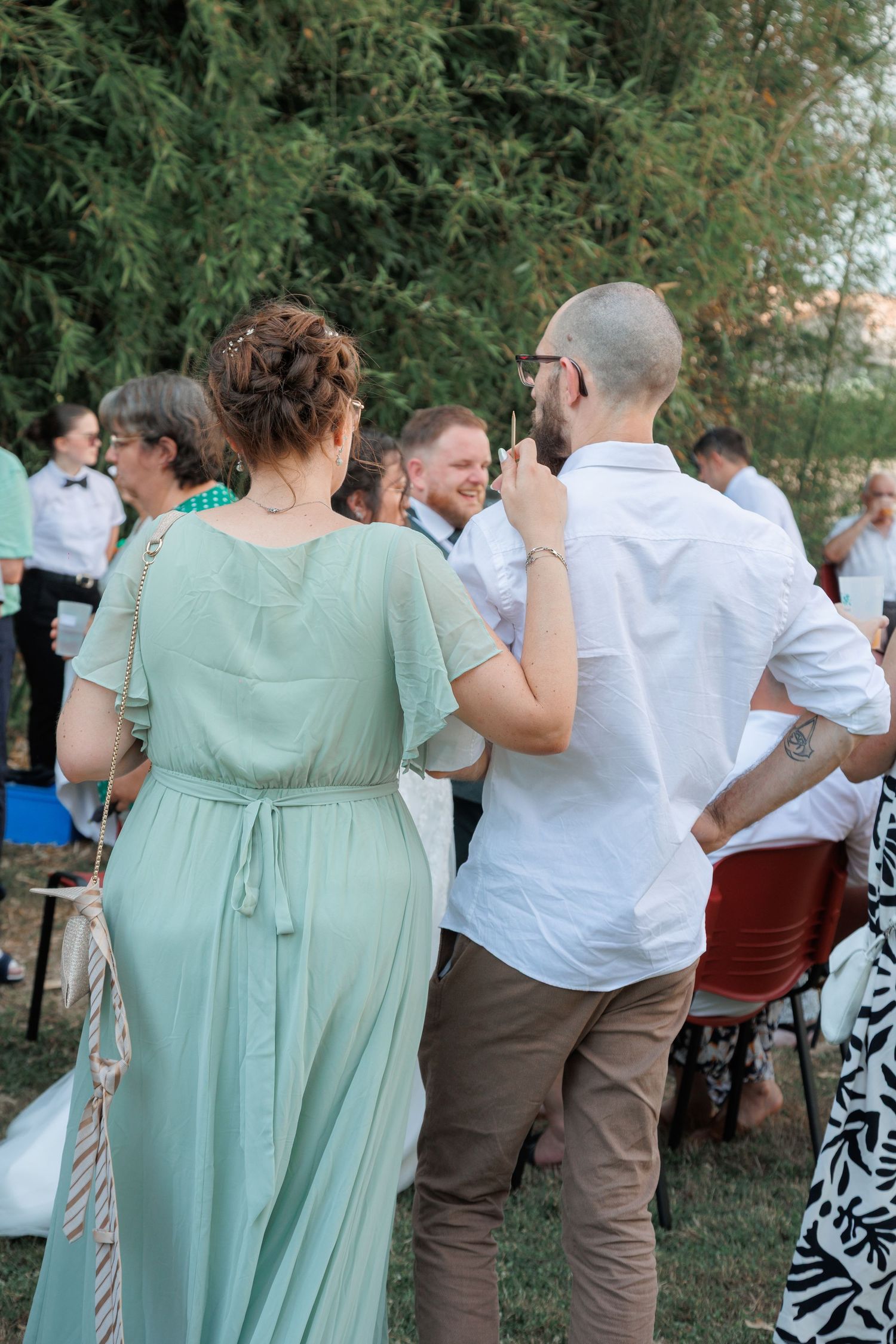 Wedding guests mingling outdoors, bridesmaid in sage green dress with bald man.
