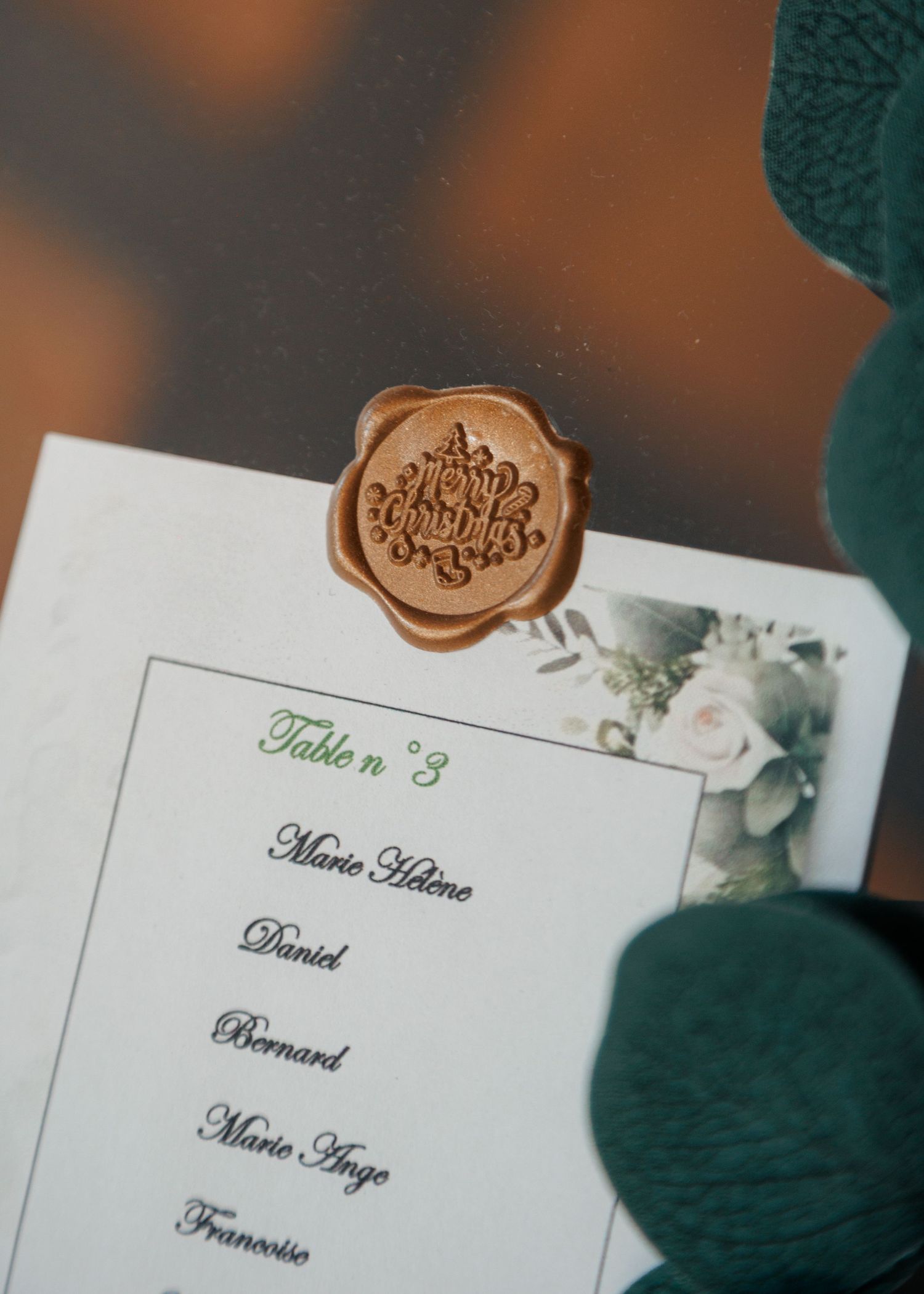 Gold wax seal on elegant wedding seating chart card listing Table 3 guests with floral watercolor design.