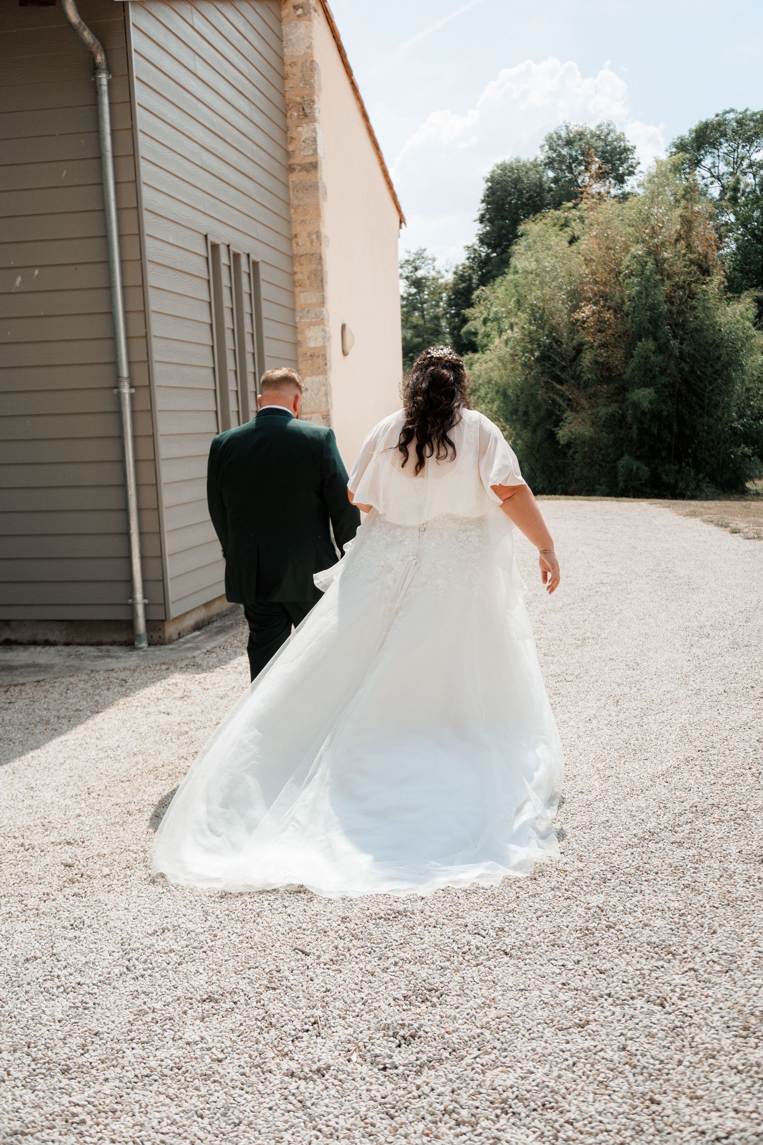 Bride and groom walking away hand in hand on gravel path, wedding dress train flowing behind her.